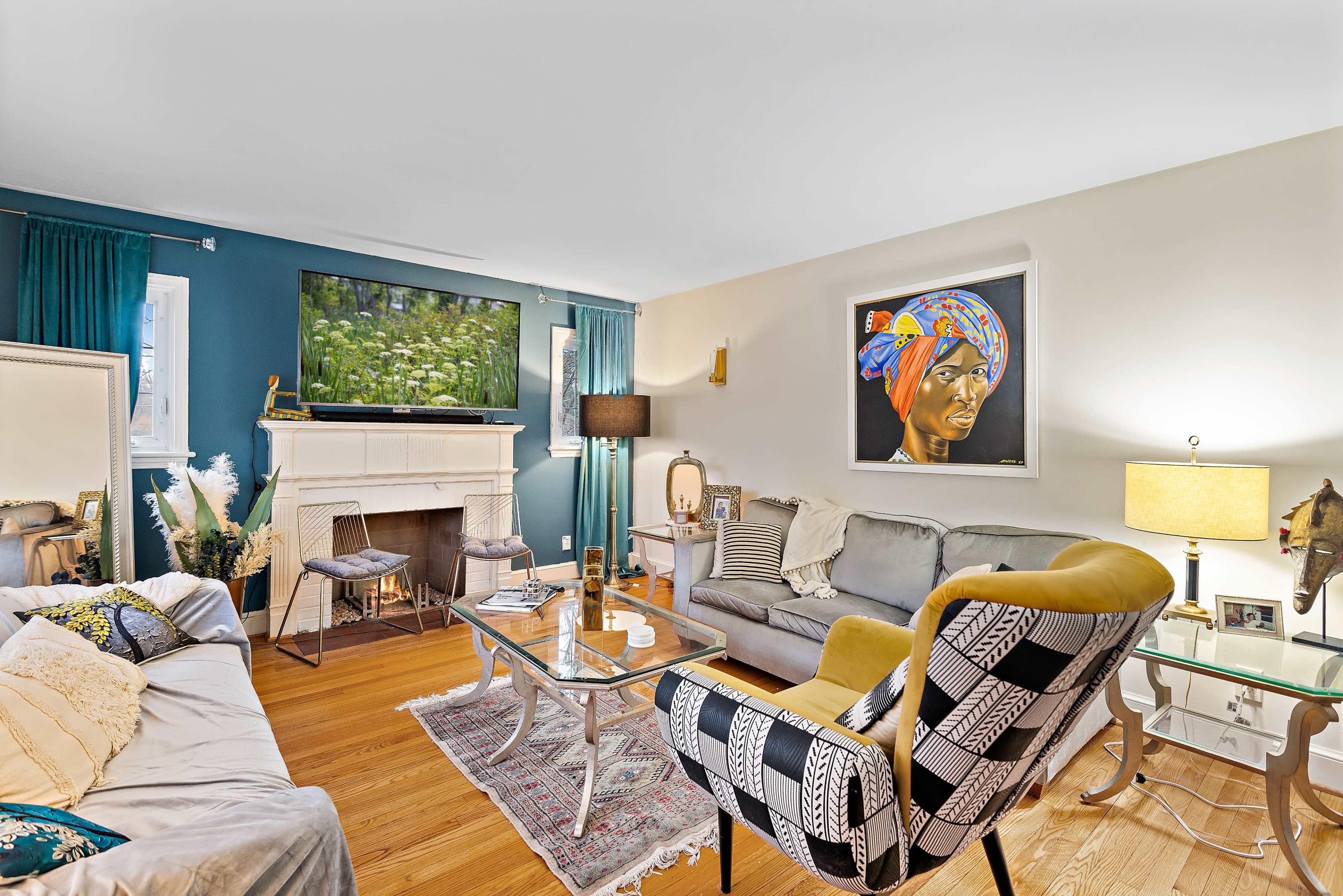 The living room features a large television mounted above a white fireplace, surrounded by various seating options and decor elements.