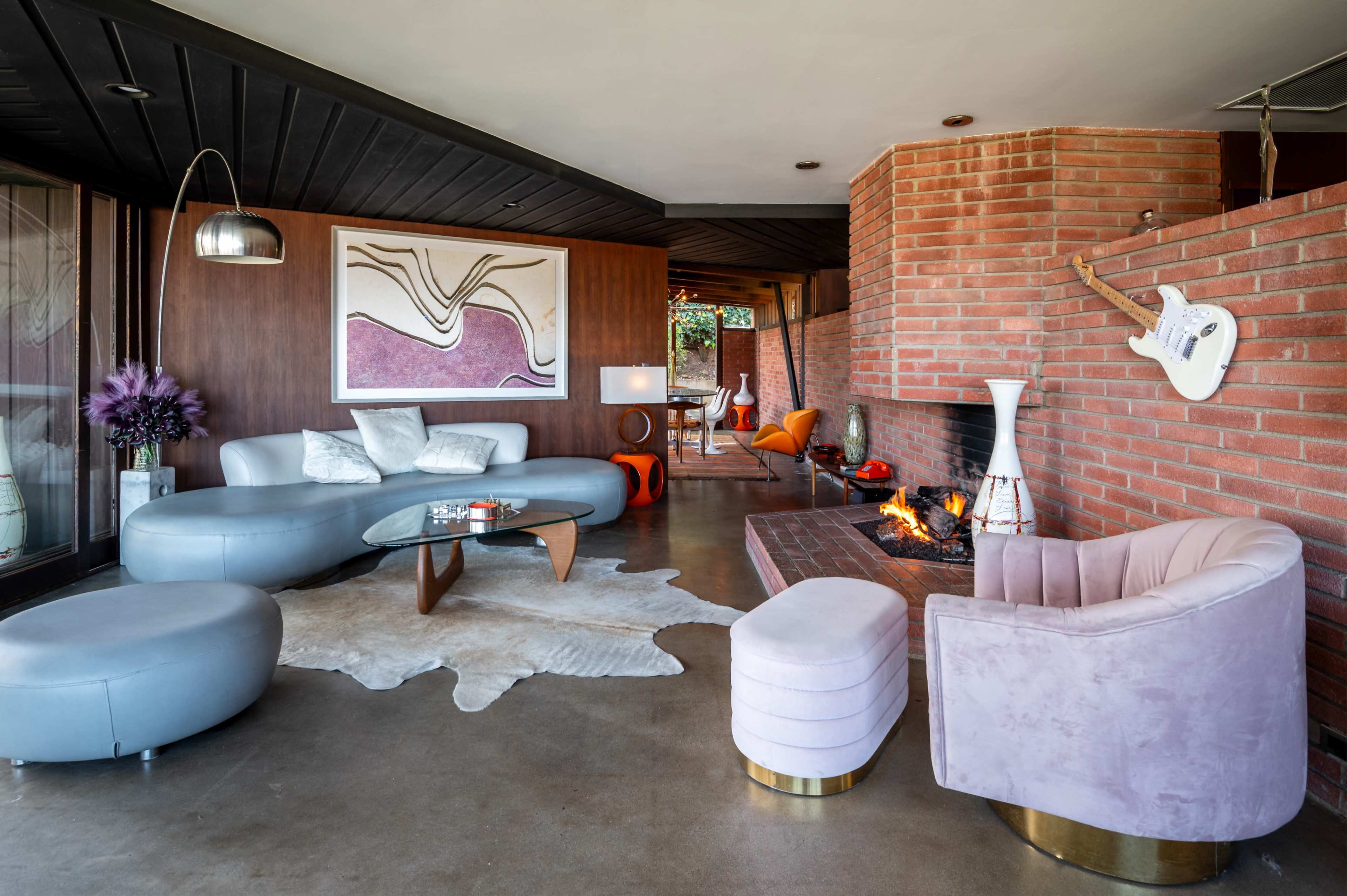 The image shows a modern living room with a combination of curved furniture, a brick fireplace, and contemporary art on the walls.