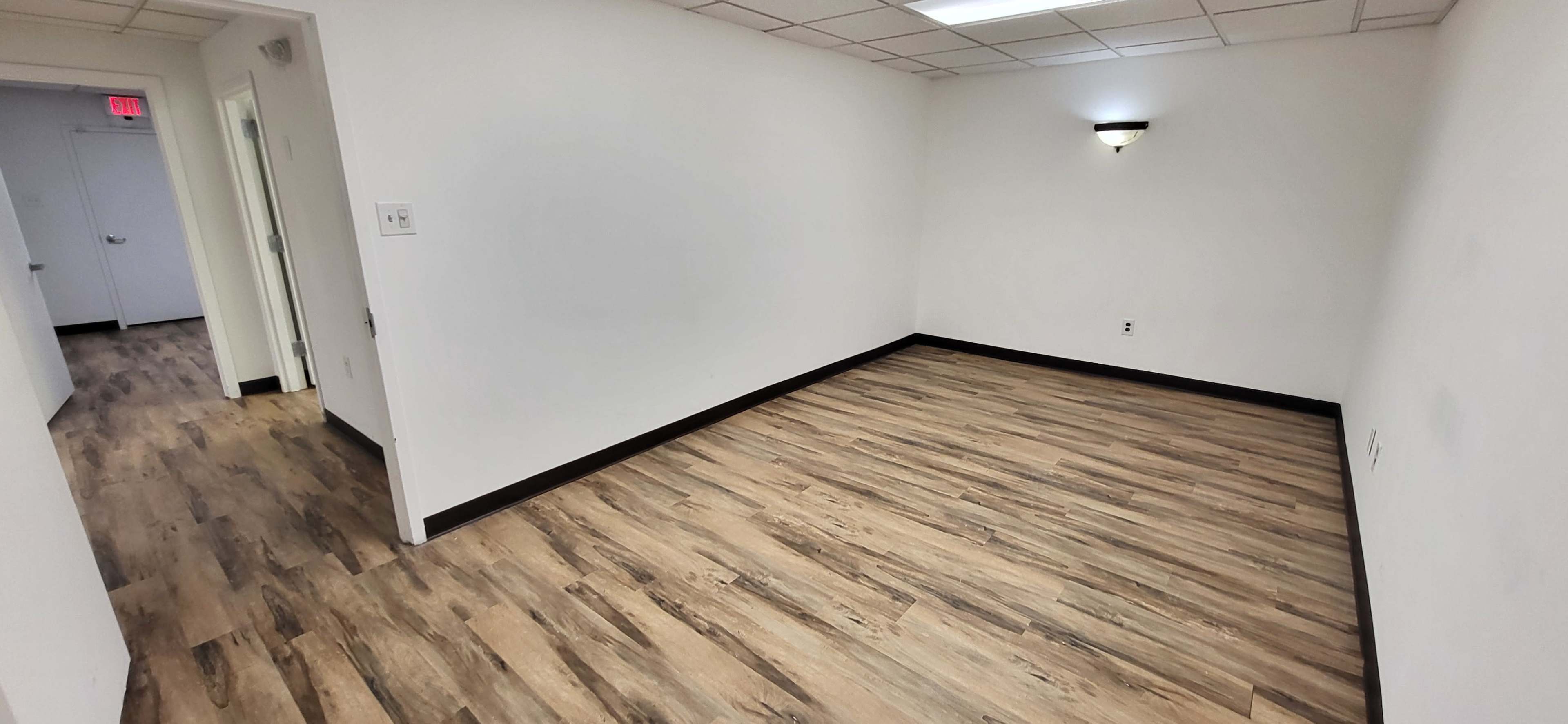 An empty room with light-colored walls and a wooden floor, featuring a single wall-mounted light fixture.