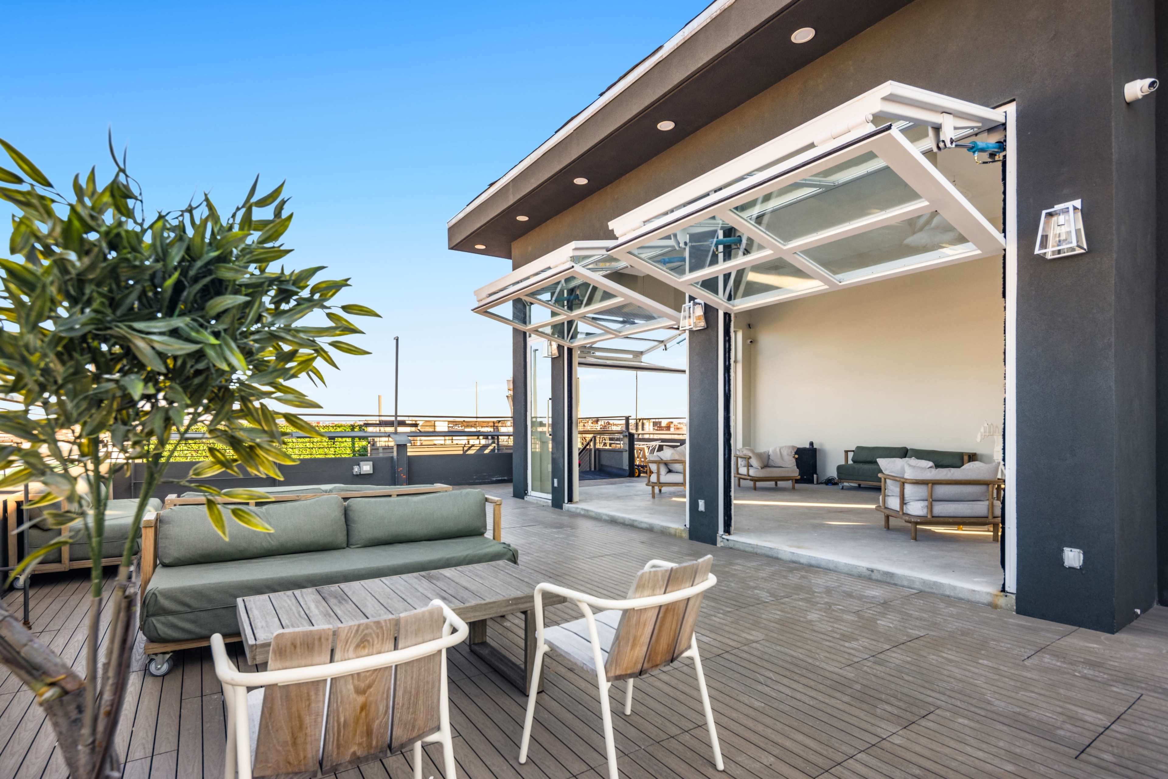 A rooftop terrace features large open glass doors, a lounge area with green and wooden furniture, and views of the surrounding skyline.