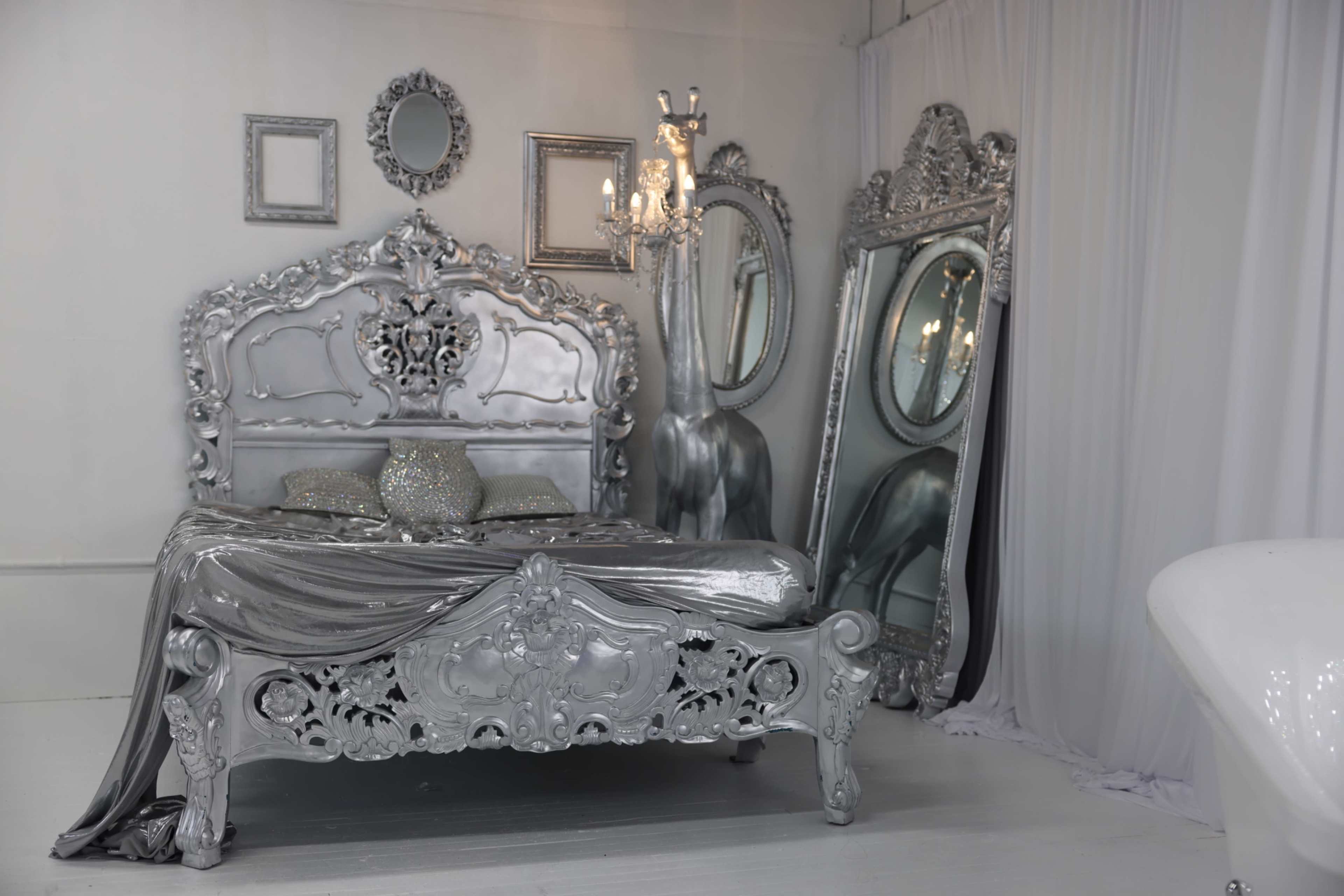 The image shows a silver-themed bedroom featuring an ornate bed, two large decorative mirrors, and a chandelier.