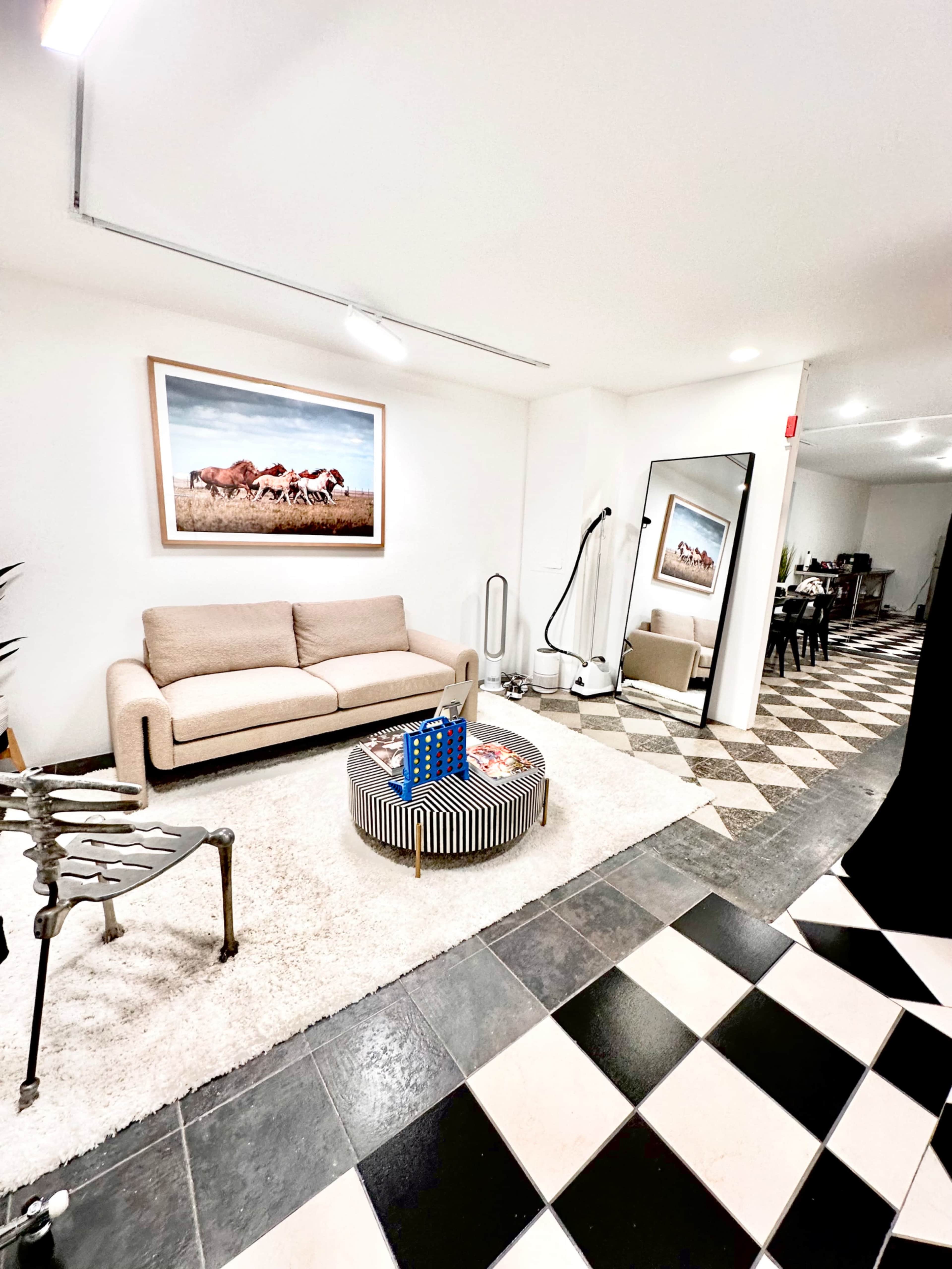 The image shows a modern indoor space with a beige sofa, a round coffee table, and a large wall mirror, featuring checkered black and white flooring.
