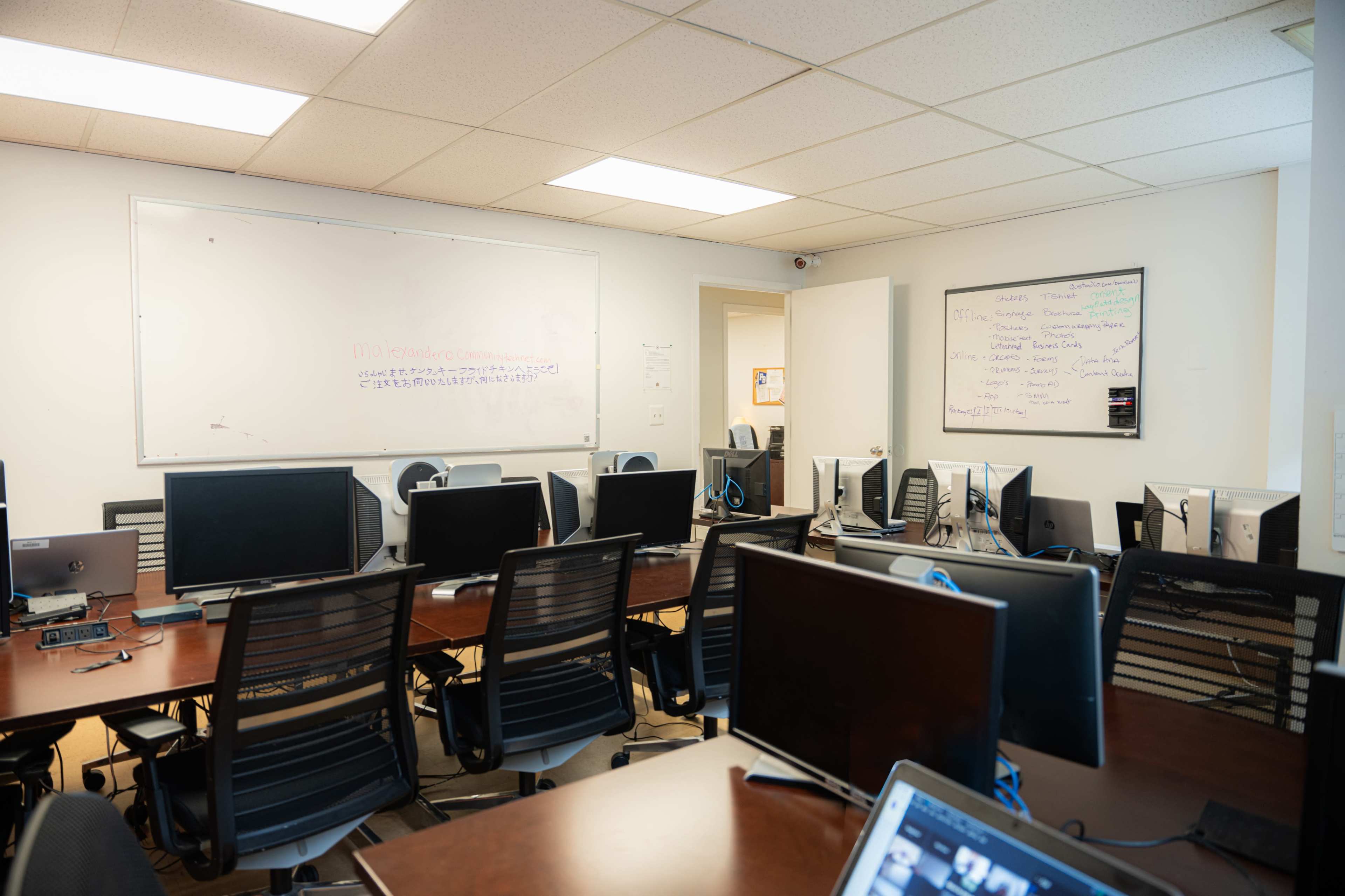 A busy office space with multiple desks equipped with computers and whiteboards on the walls.
