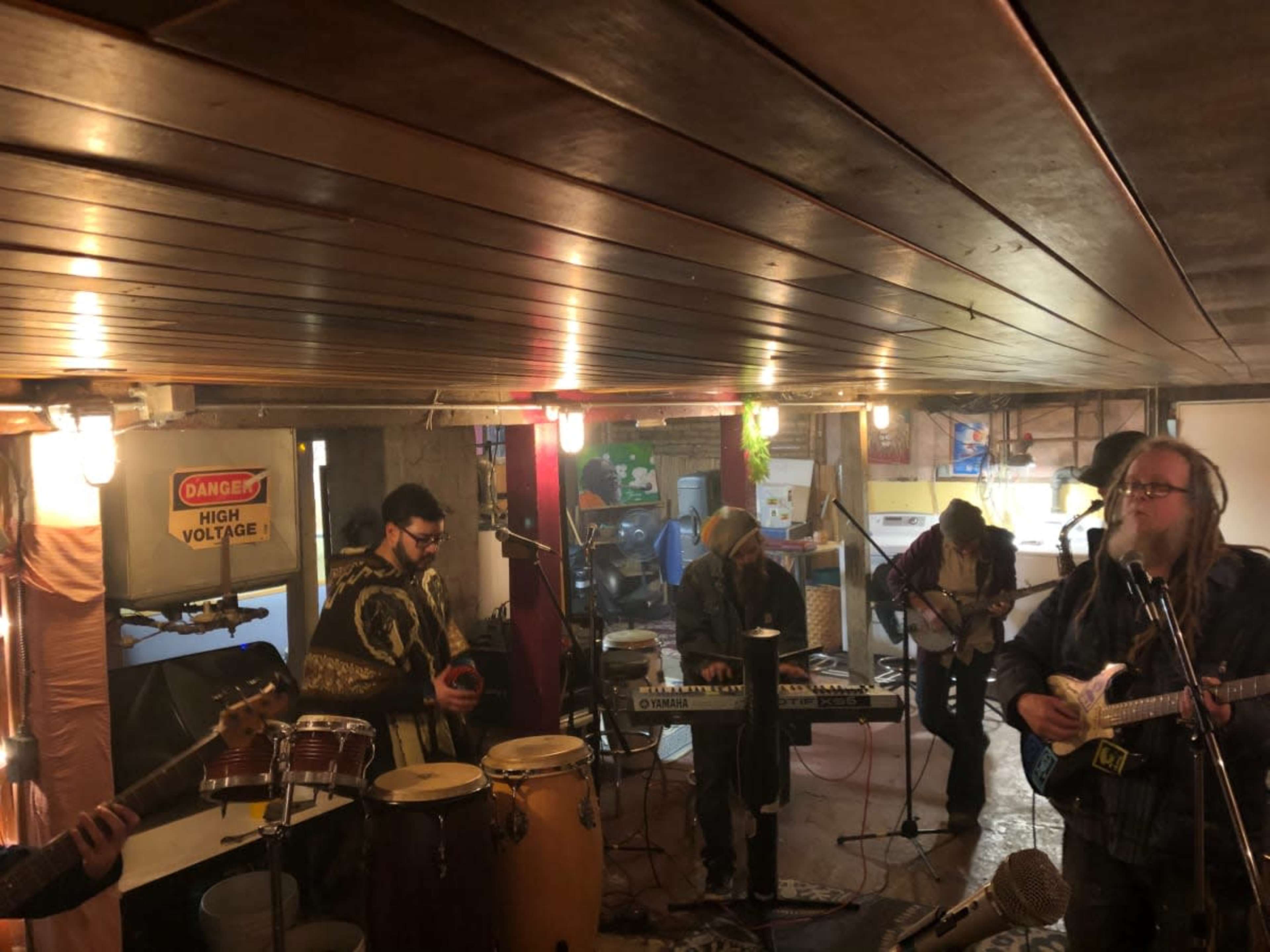 A group of musicians plays various instruments in a dimly lit basement studio.