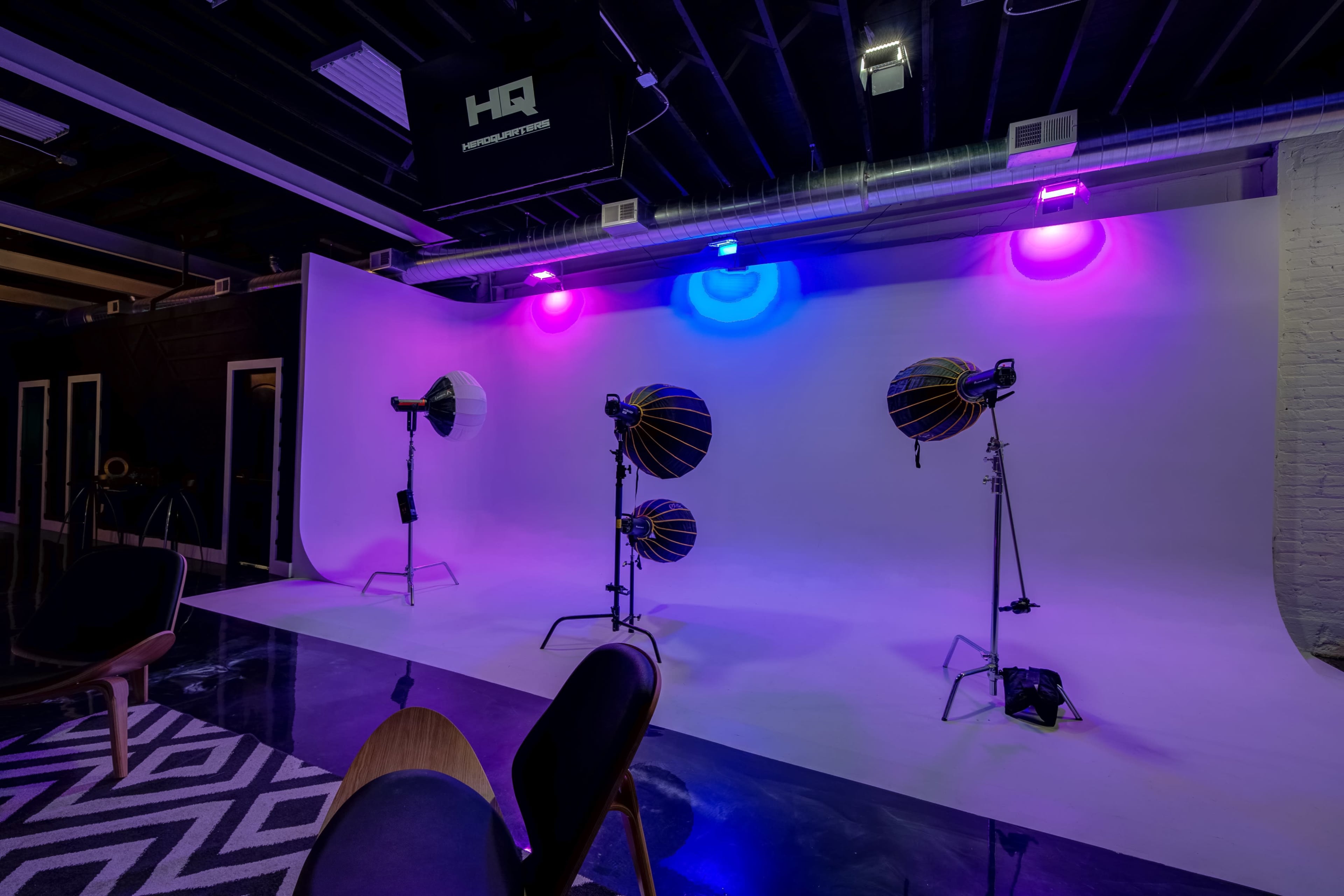 A photography studio features a white backdrop illuminated by colored lights and equipped with multiple studio lights and softboxes.
