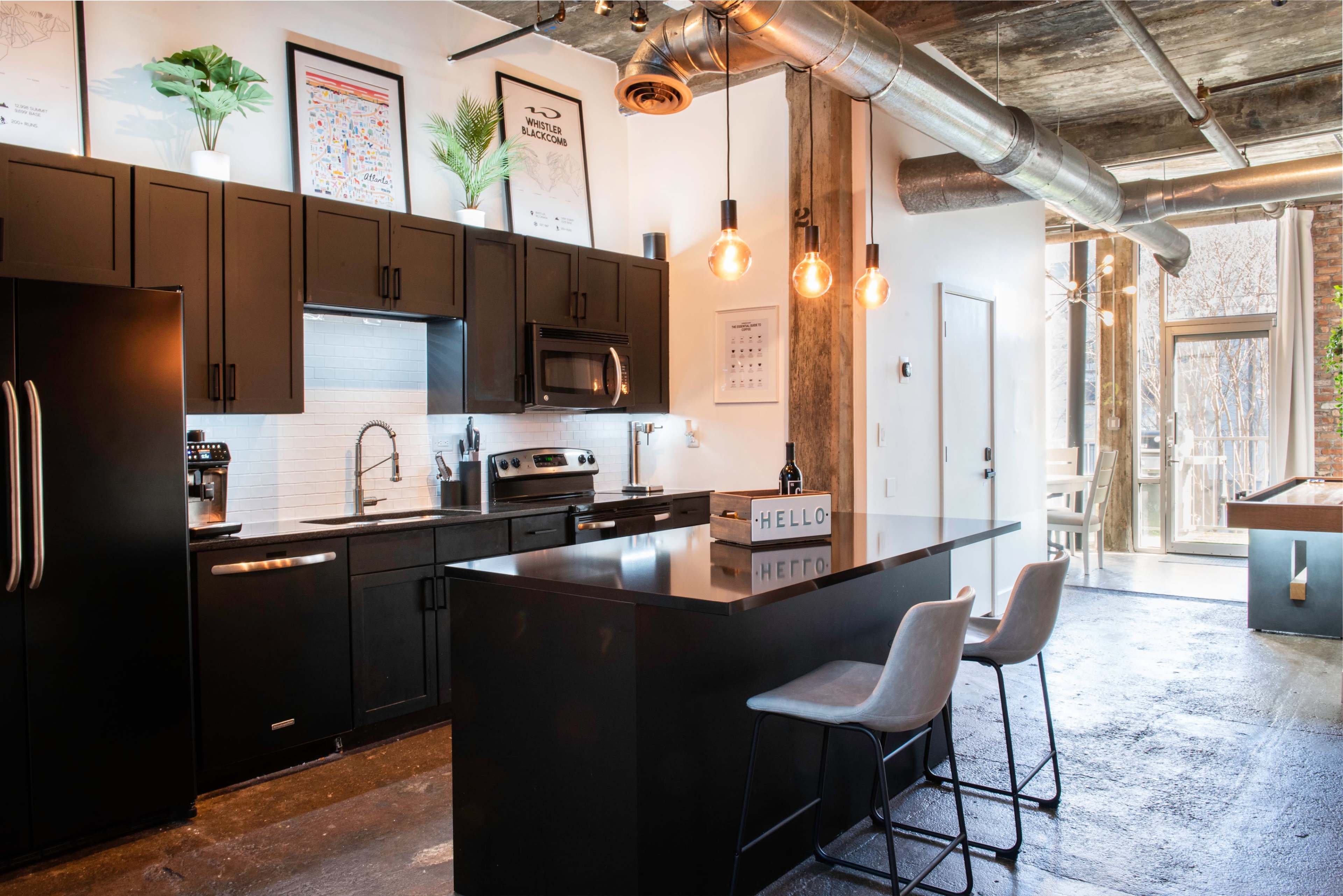 A modern kitchen with black cabinetry, stainless steel appliances, and an island with bar stools, illuminated by pendant lights.