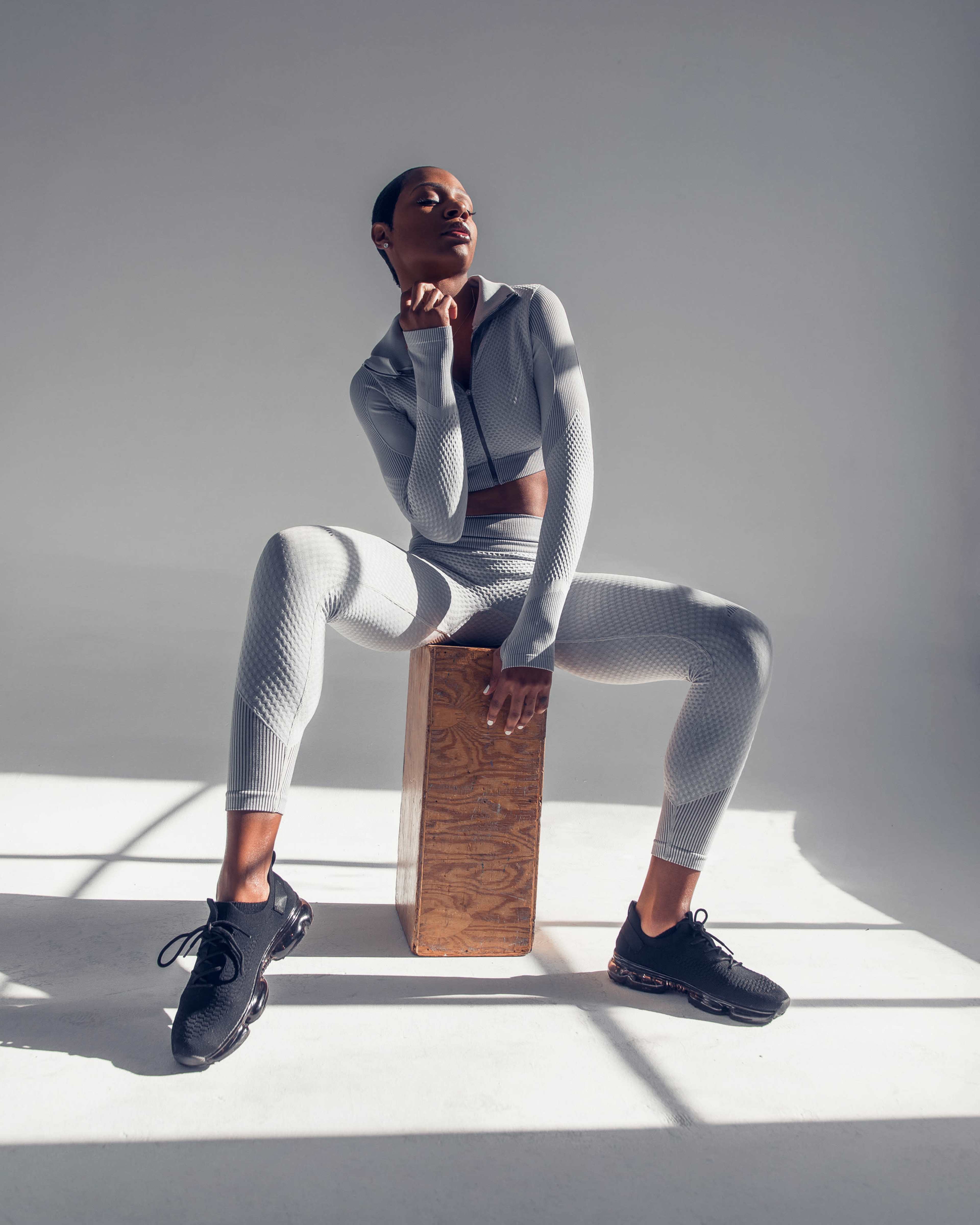 A person in athletic wear sits on a wooden block in a well-lit, minimalist setting.