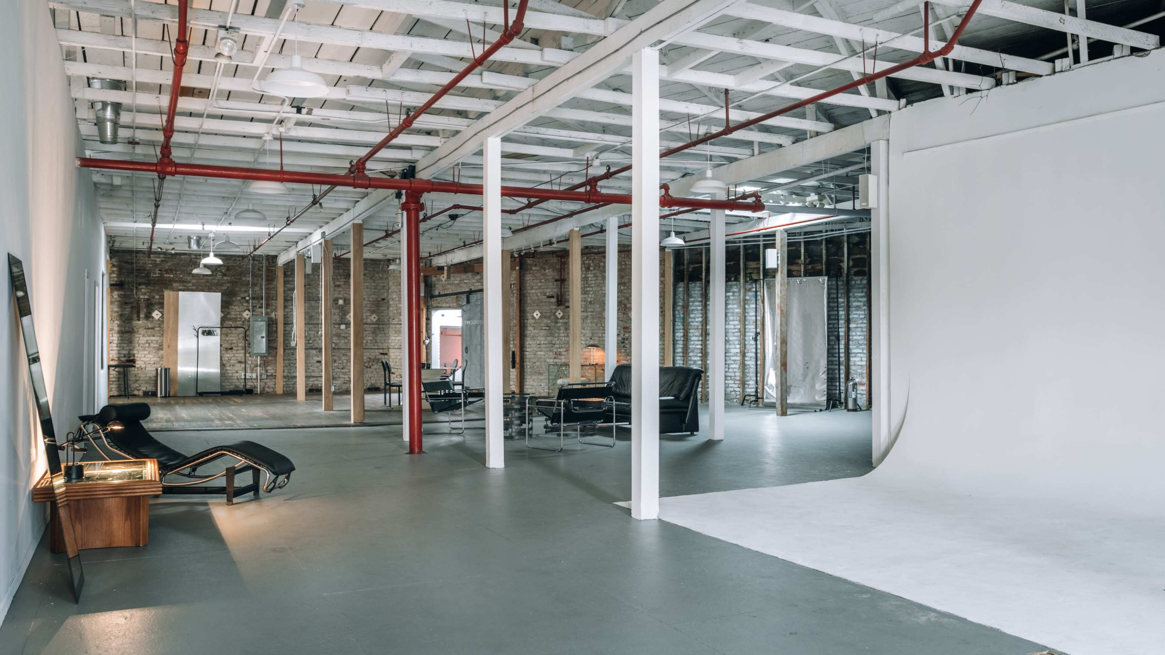 An industrial-style studio space featuring exposed brick walls, high ceilings with visible beams, and various seating arrangements.