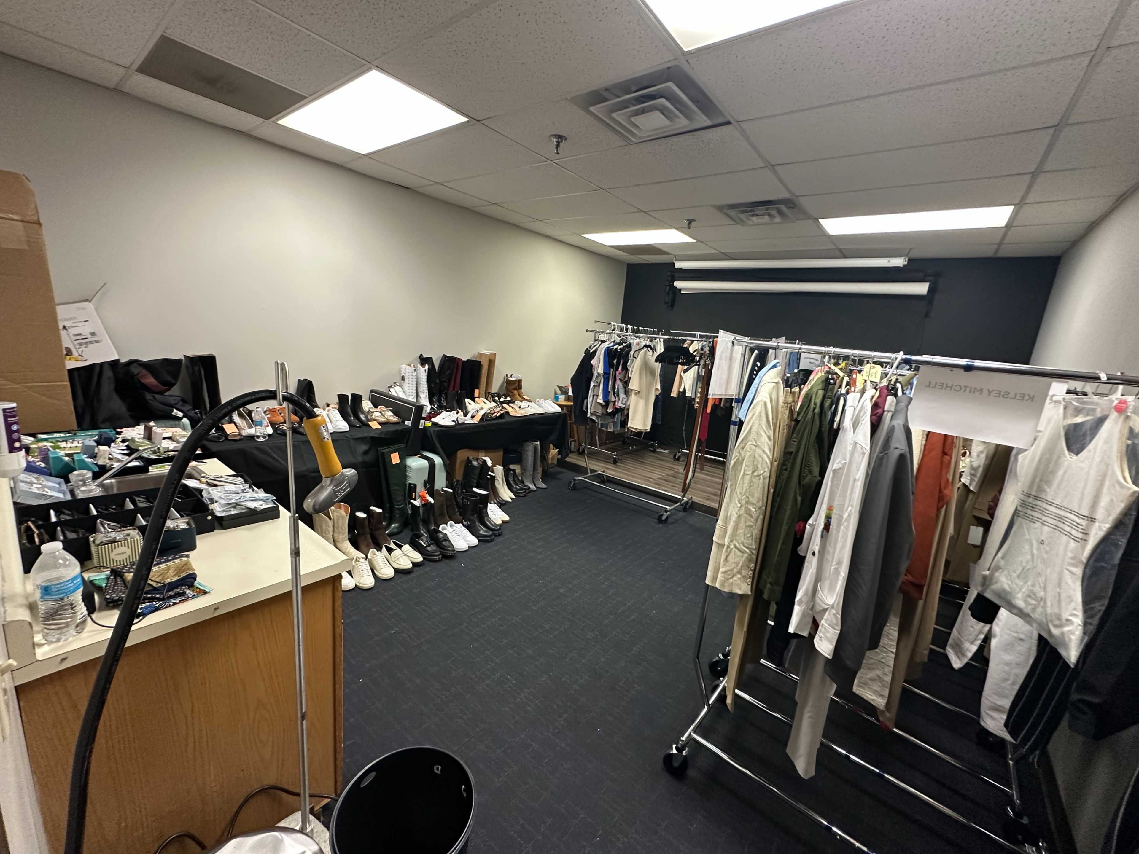 The image shows a spacious room filled with clothing racks and various shoes arranged neatly along the walls.