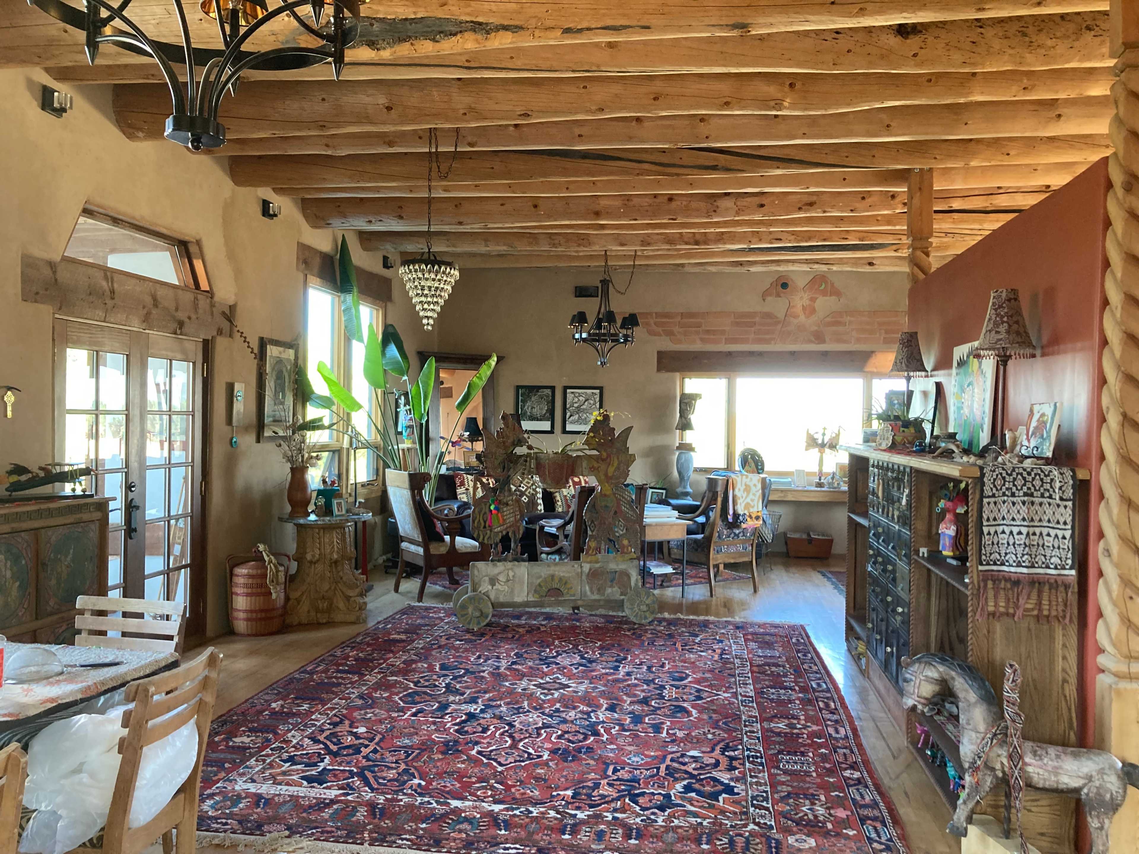 A spacious interior featuring wood-beamed ceilings, rustic furniture, and a large area rug, with a dining area visible in the background.
