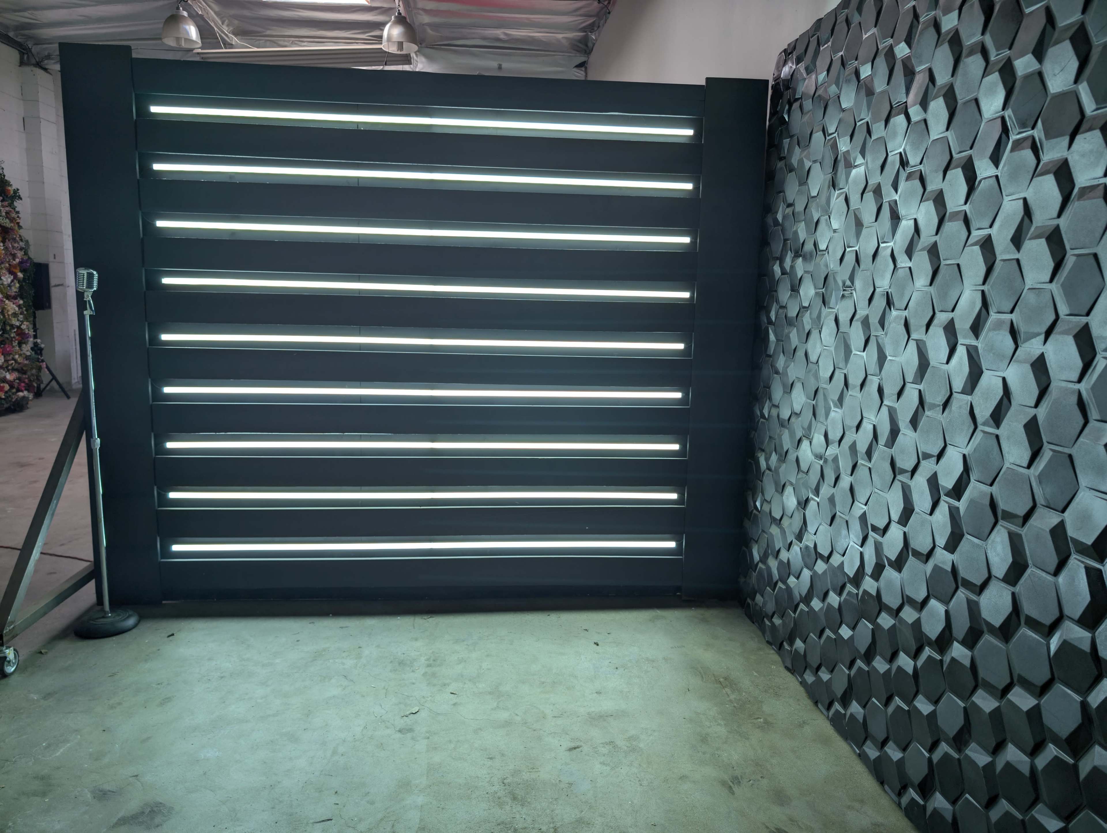 The image shows a modern interior space featuring a wall with horizontal LED light strips and a textured hexagonal panel on the adjacent wall.