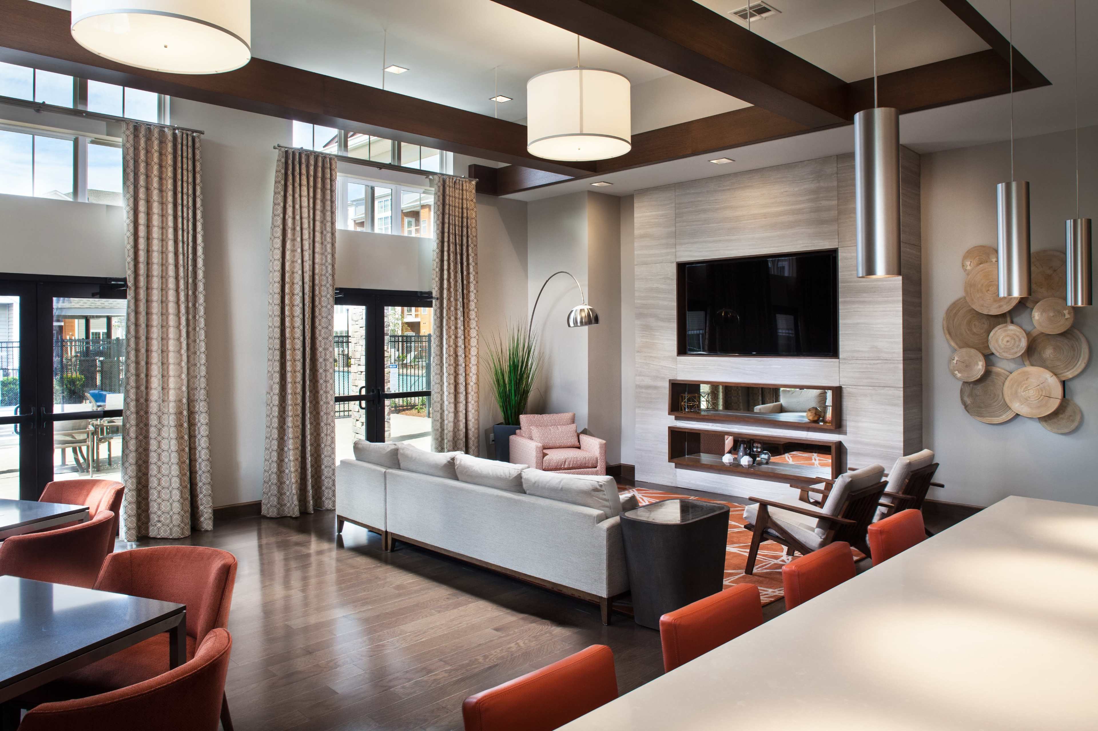 A modern living room with a large television mounted on the wall, a sectional sofa, and a dining area featuring red chairs.