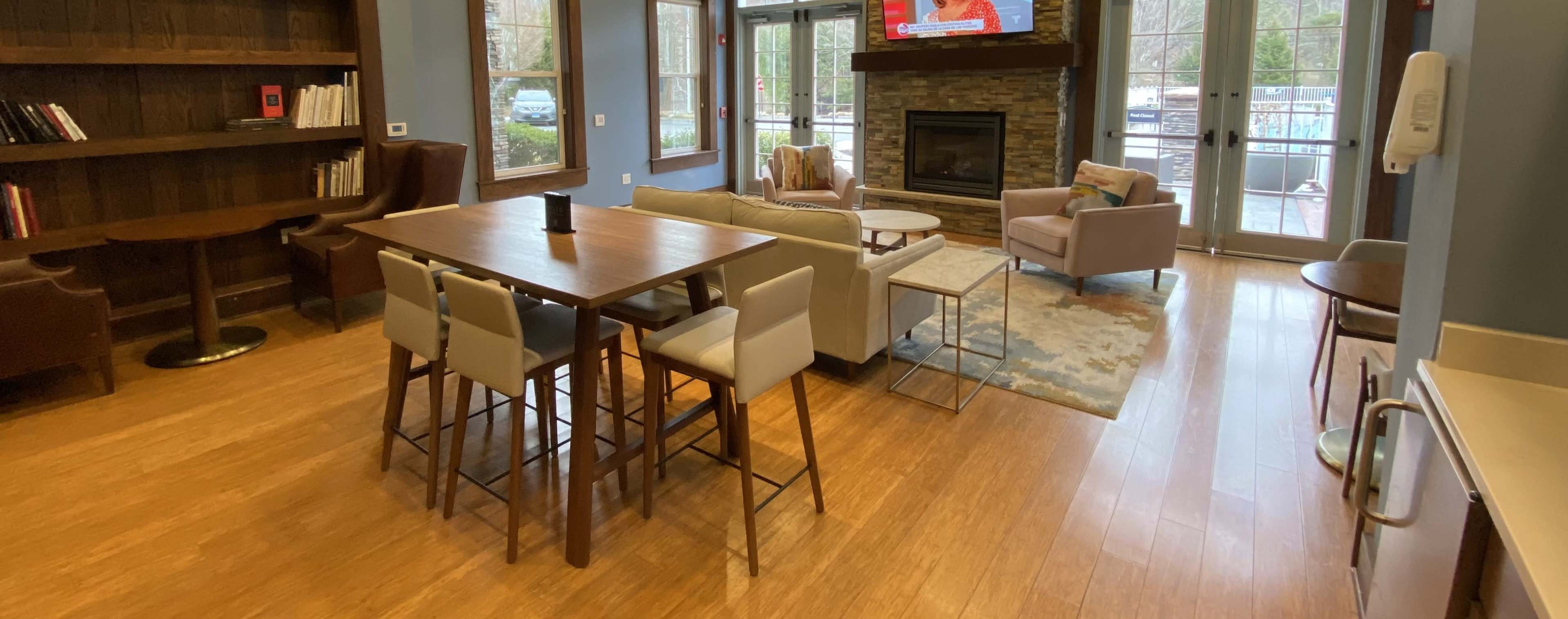 A spacious indoor lounge area with a wooden table, high chairs, a comfortable seating arrangement, a stone fireplace, and large windows providing natural light.