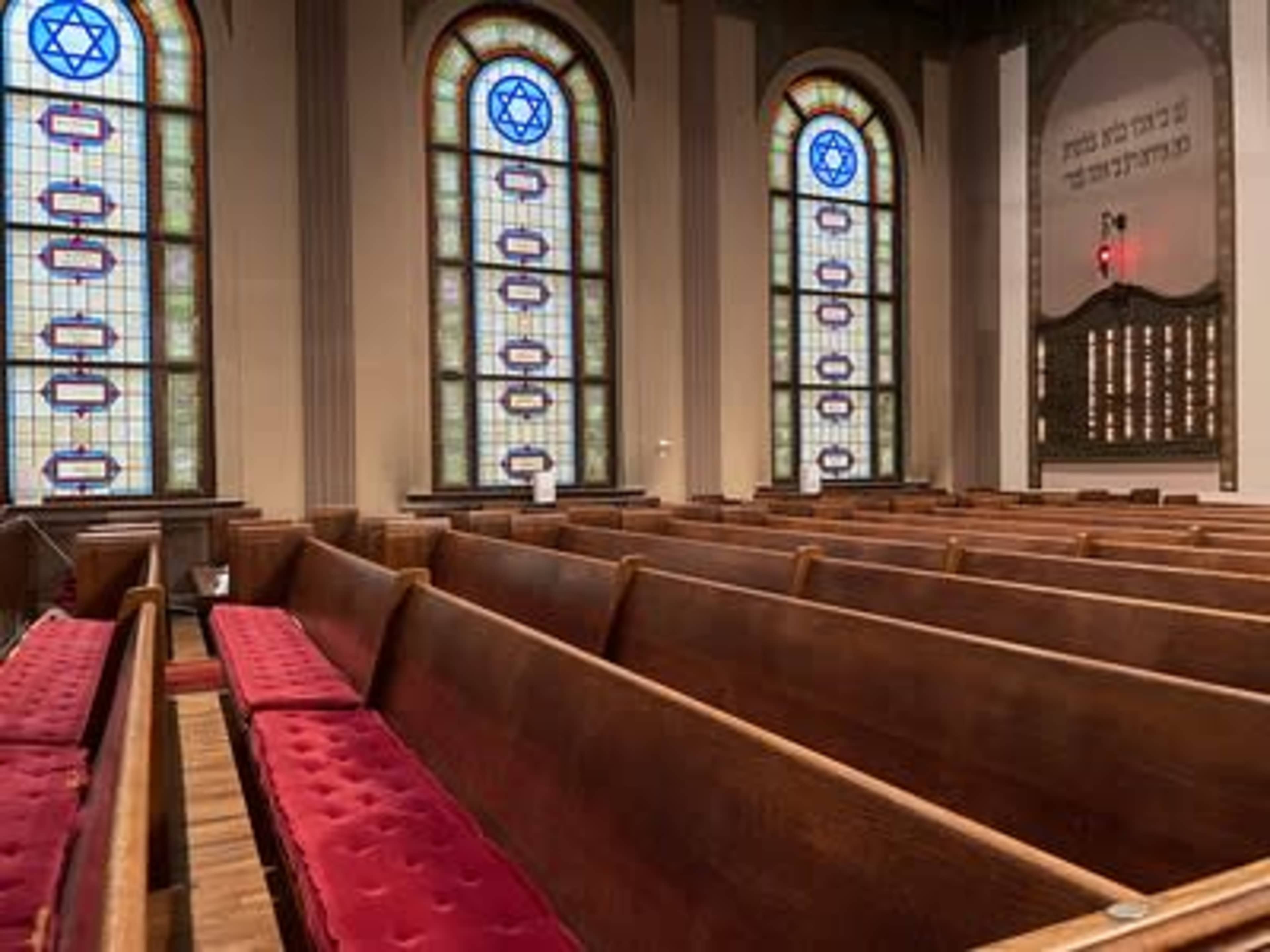 The interior of a synagogue with wooden pews and stained glass windows featuring Star of David symbols.