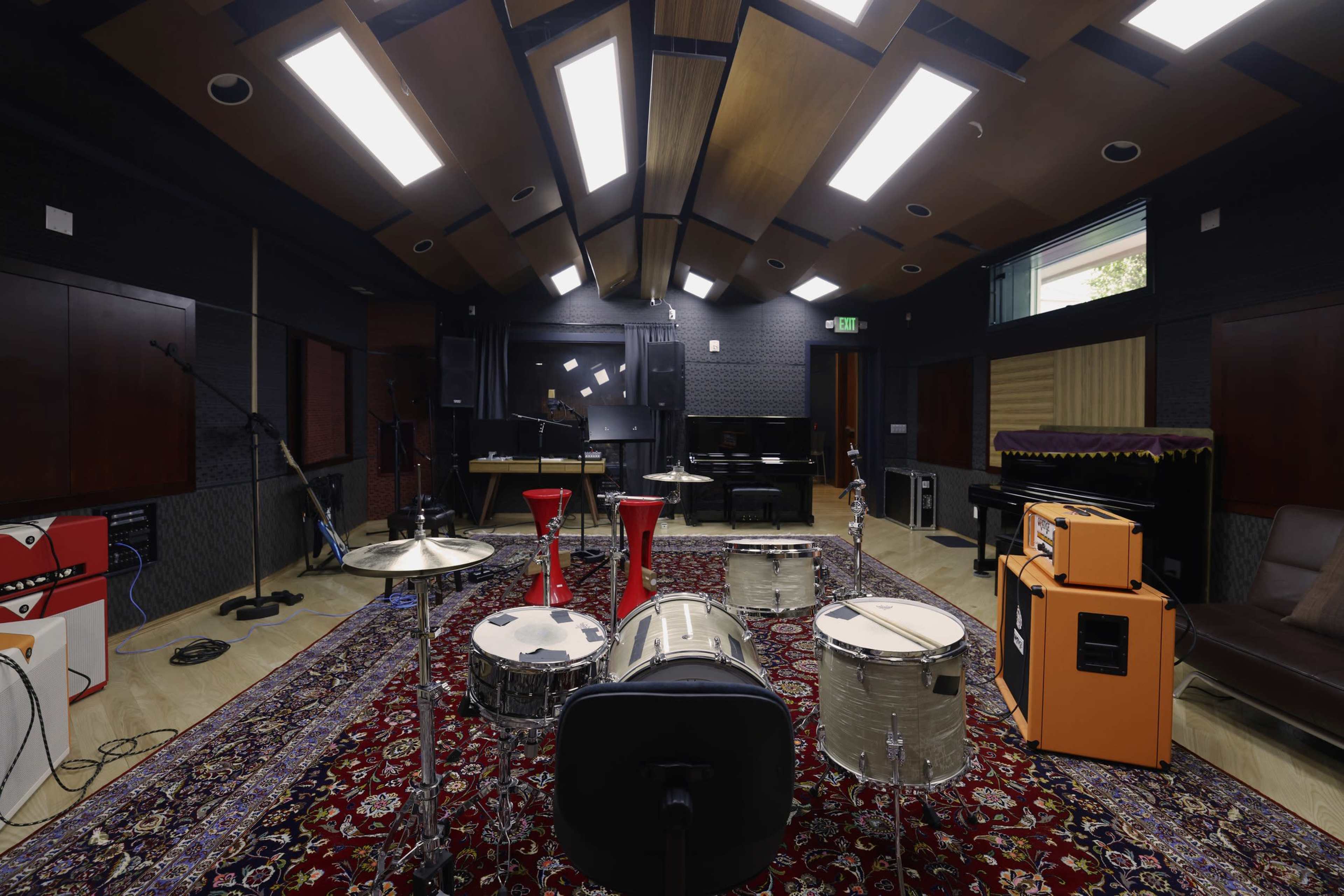 A music recording studio featuring various instruments, including drums and amplifiers, arranged on a patterned rug with a visually interesting ceiling design.