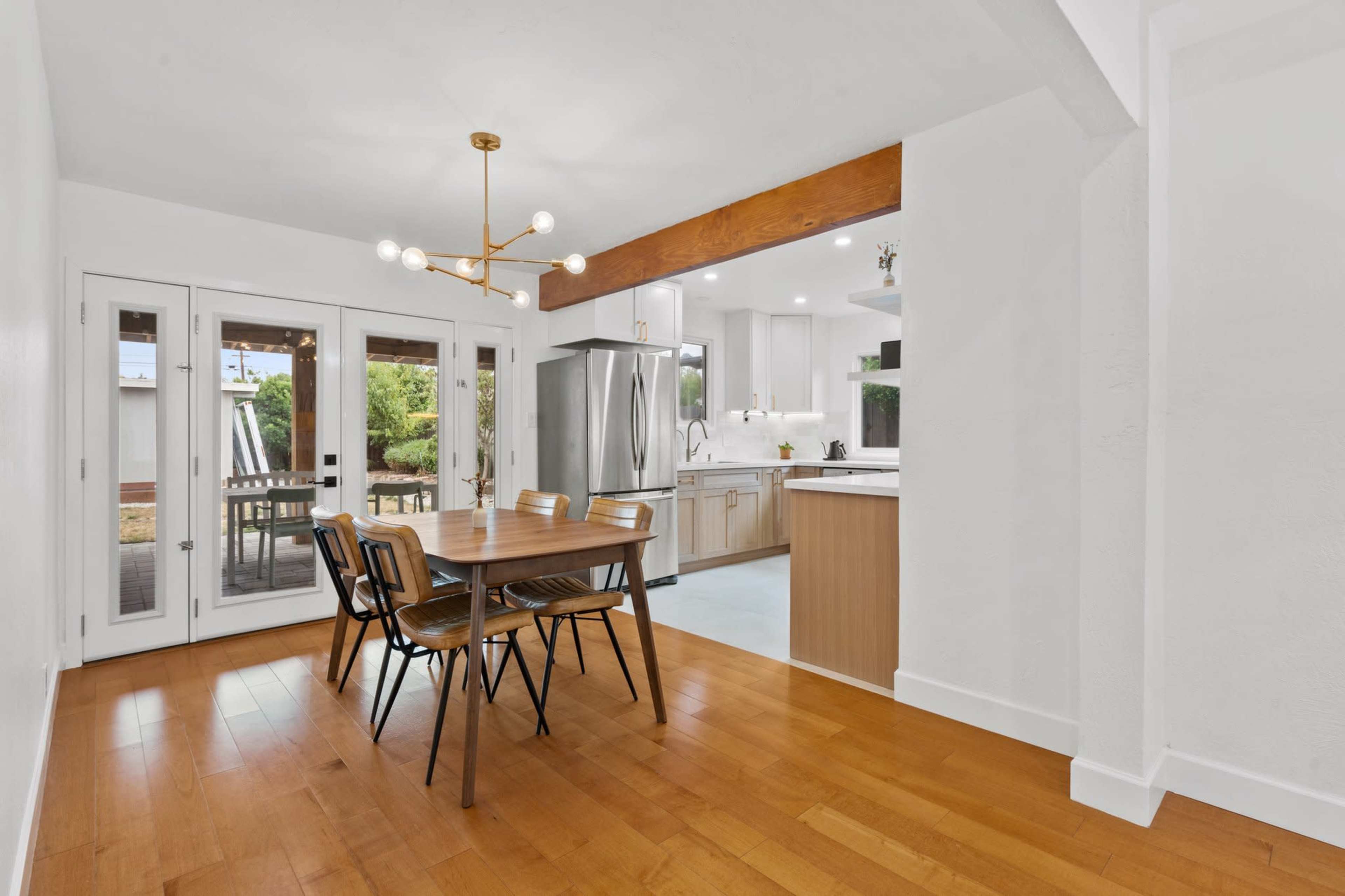 A dining area features a wooden table with chairs, adjacent to a kitchen with stainless steel appliances and open access to an outdoor space through glass doors.