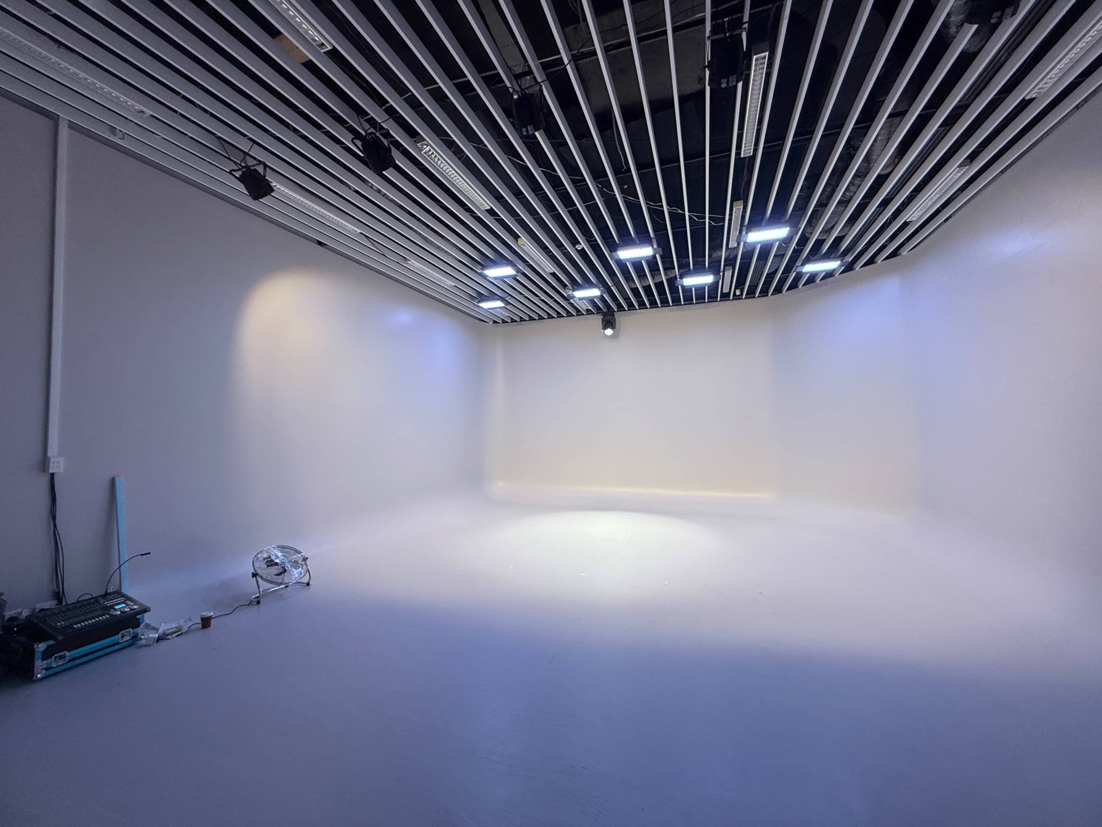 The image shows an empty studio space with a smooth white floor and walls, illuminated by overhead lights.