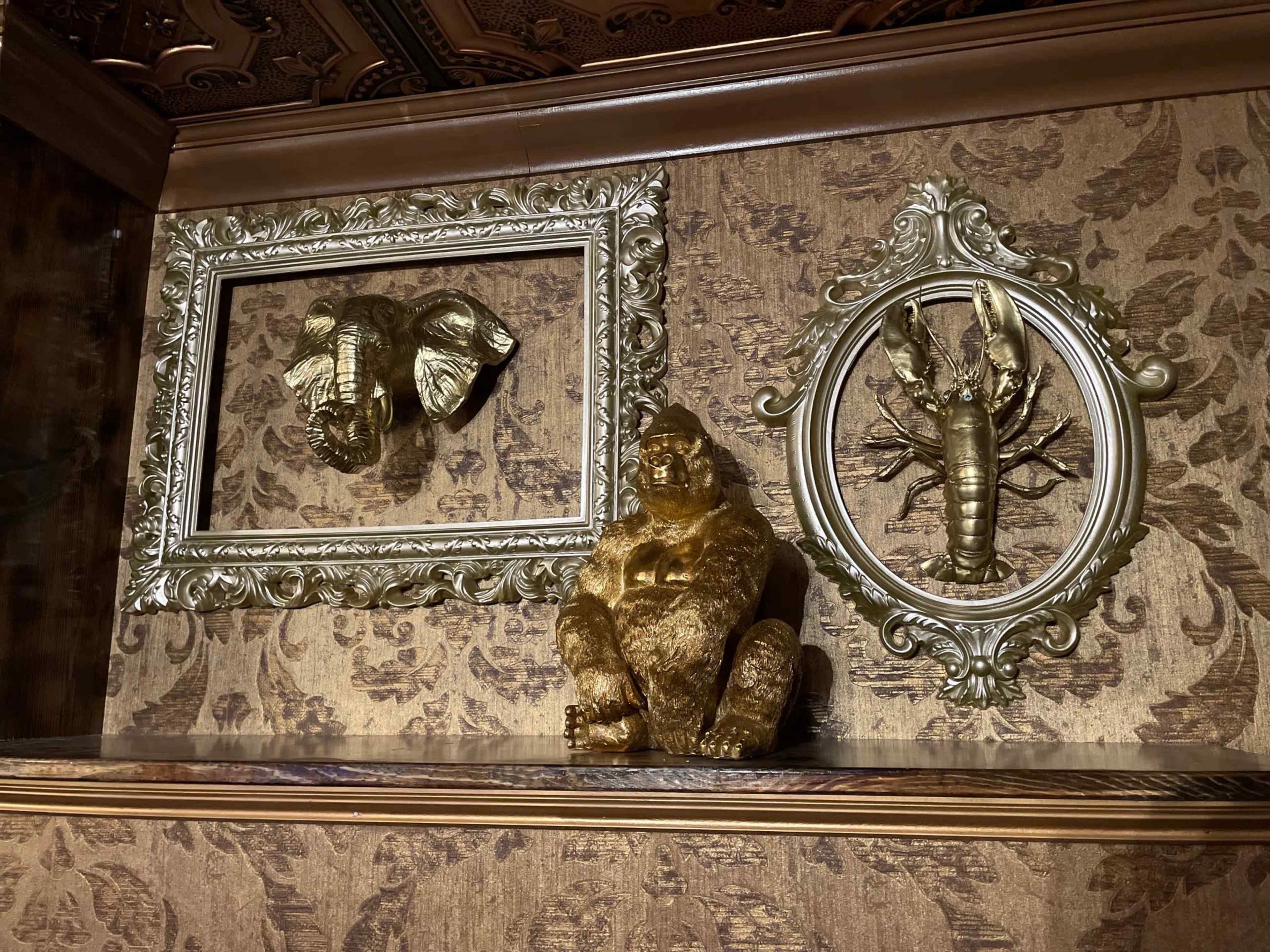 A decorative wall with a gold statue of a gorilla, two framed wall art pieces of an elephant and a lobster, all set against a patterned wallpaper.
