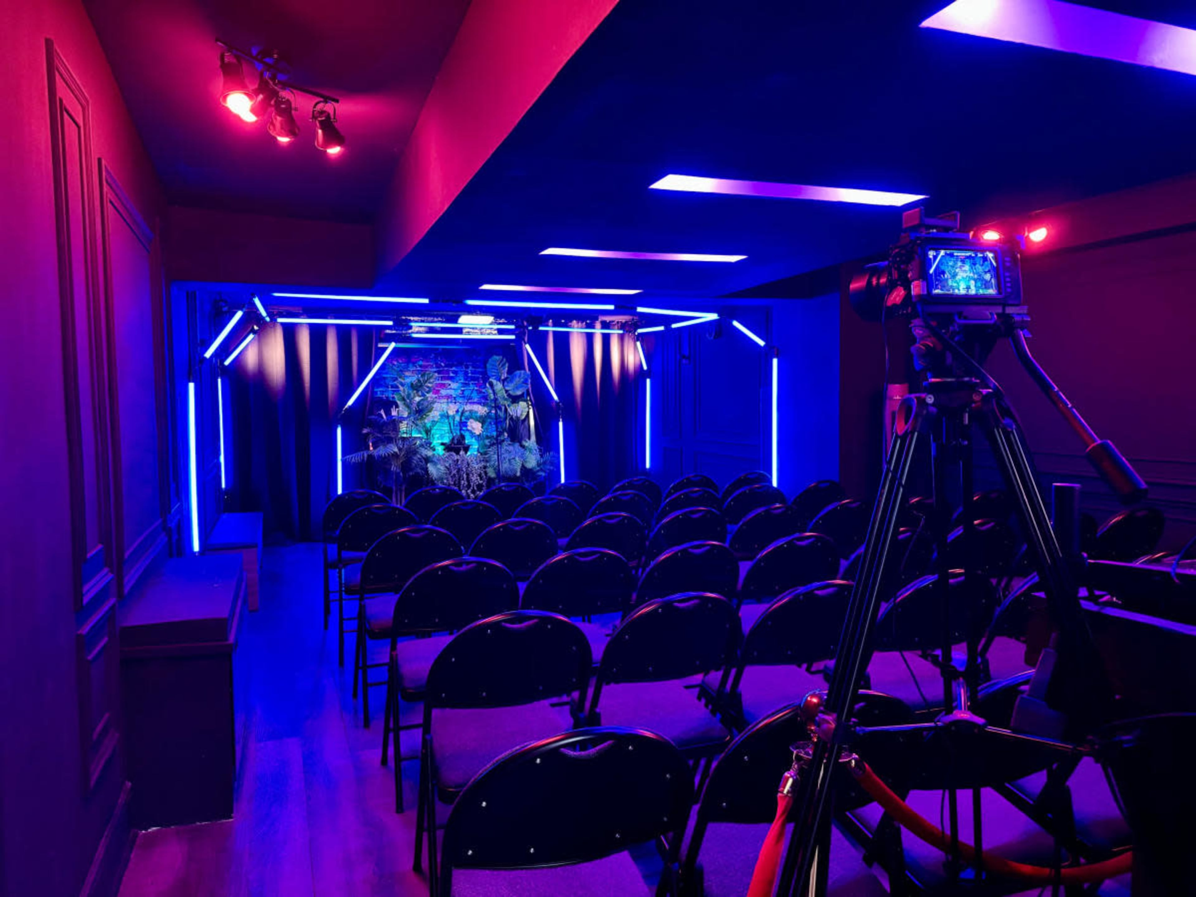 A small performance space is set up with rows of chairs facing a brightly lit stage adorned with colorful lights and a decorative backdrop.