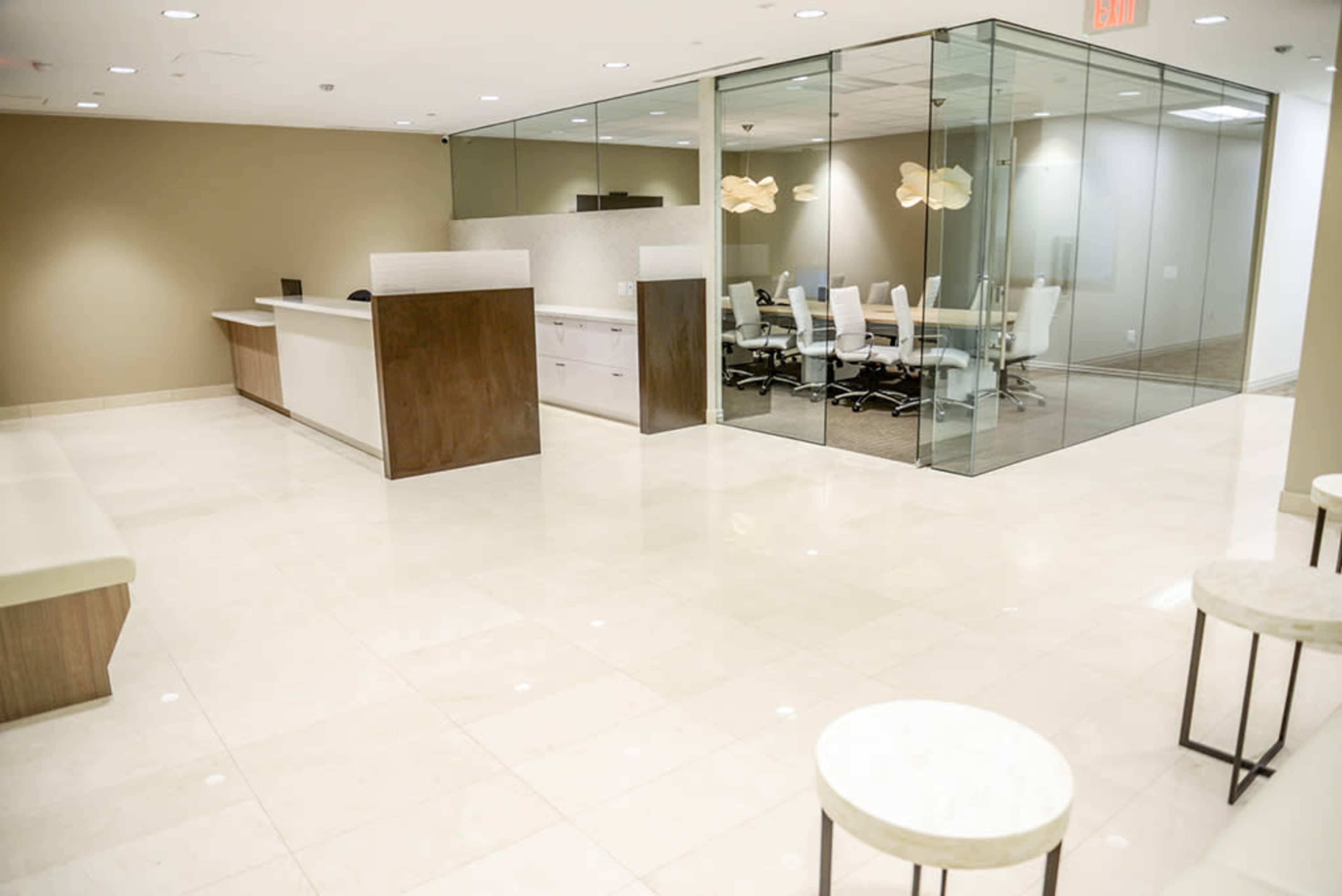A modern office lobby features white tiled flooring, a reception desk, and a glass conference room with a table and chairs.