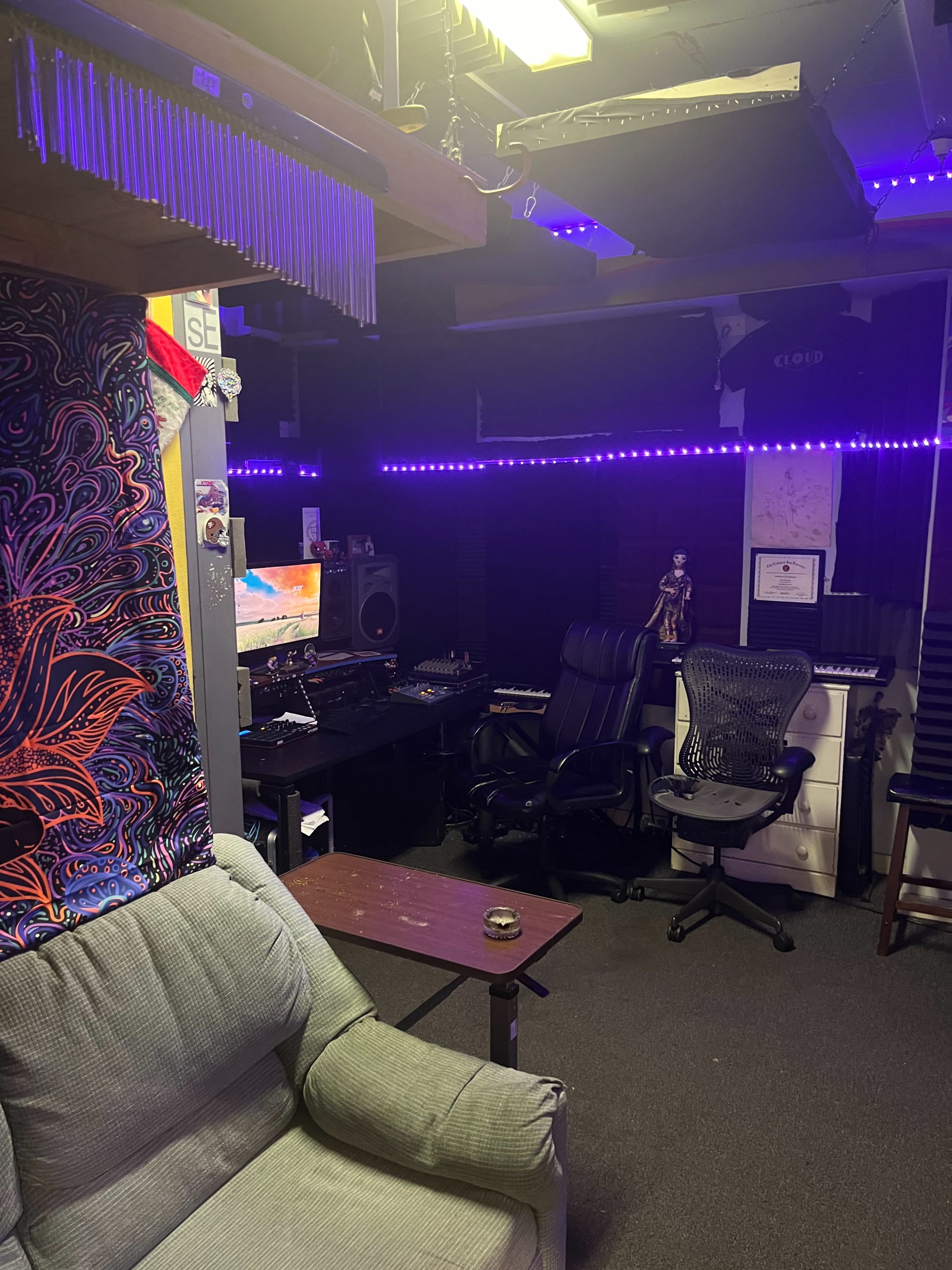 A music production studio with a couch, two office chairs, a computer desk, and colorful LED lighting.