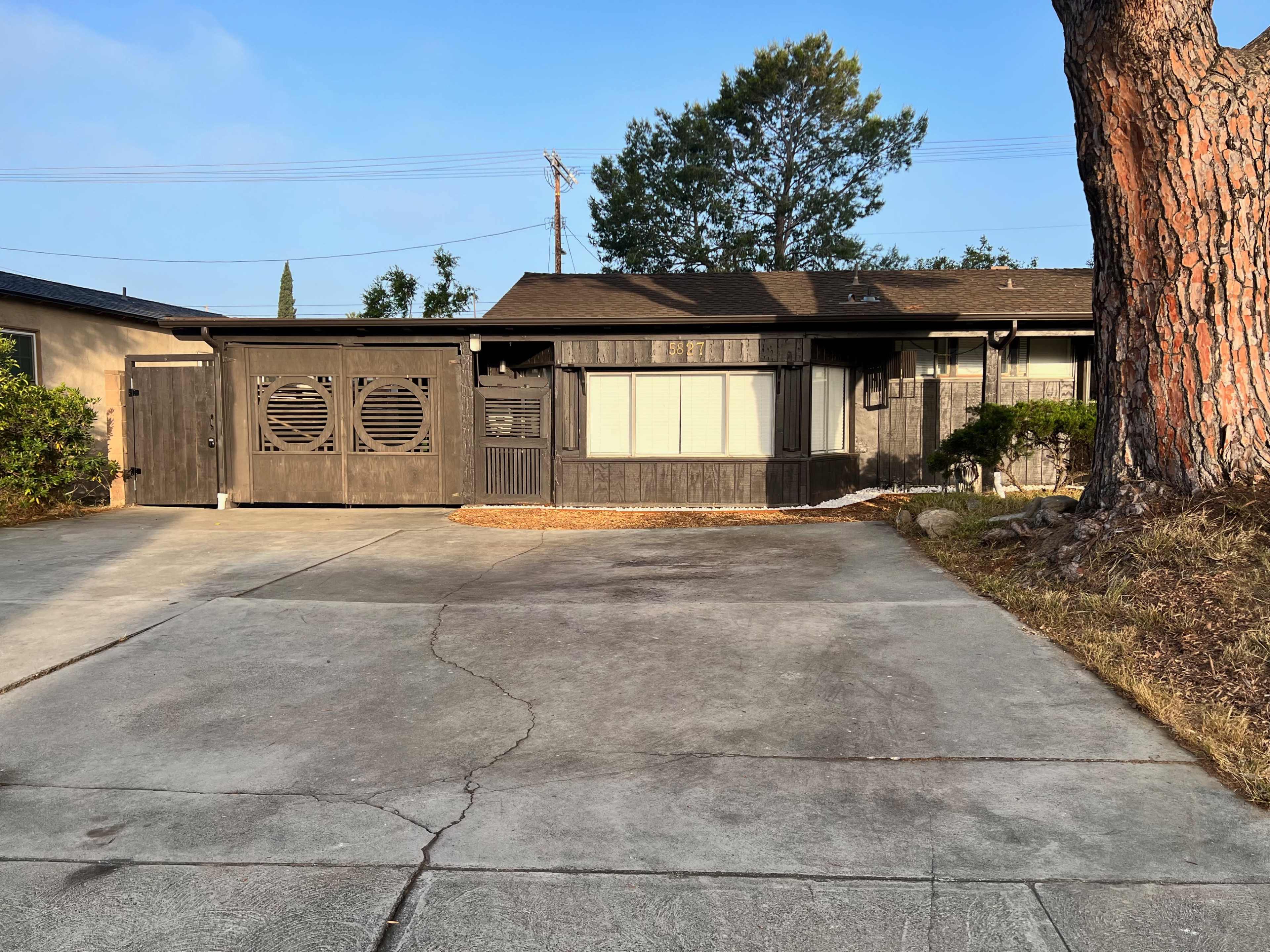 A single-story house with a wooden facade and a square driveway lined with concrete.