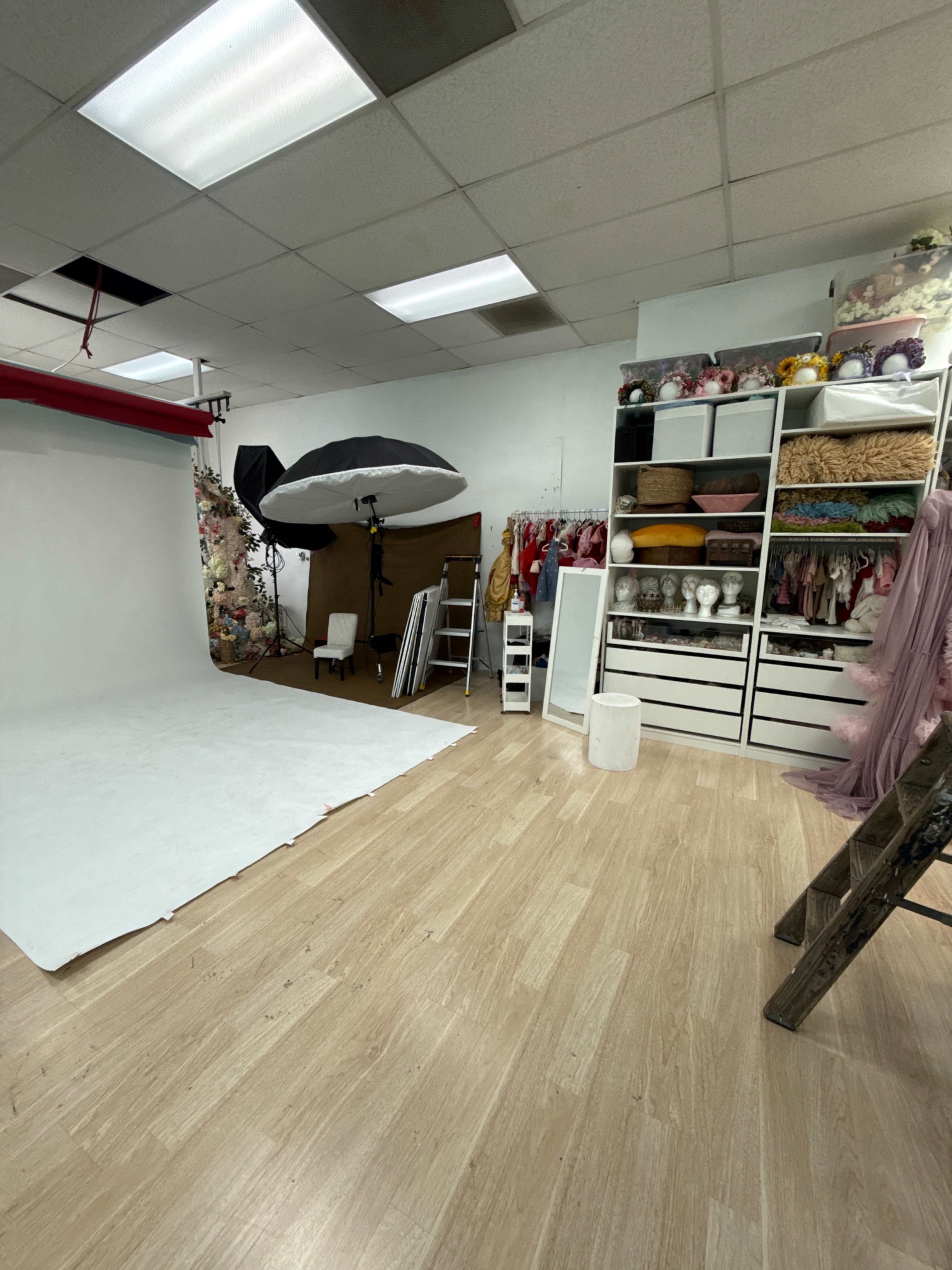A photography studio features a white backdrop, various props, and organized shelves with costumes and accessories.