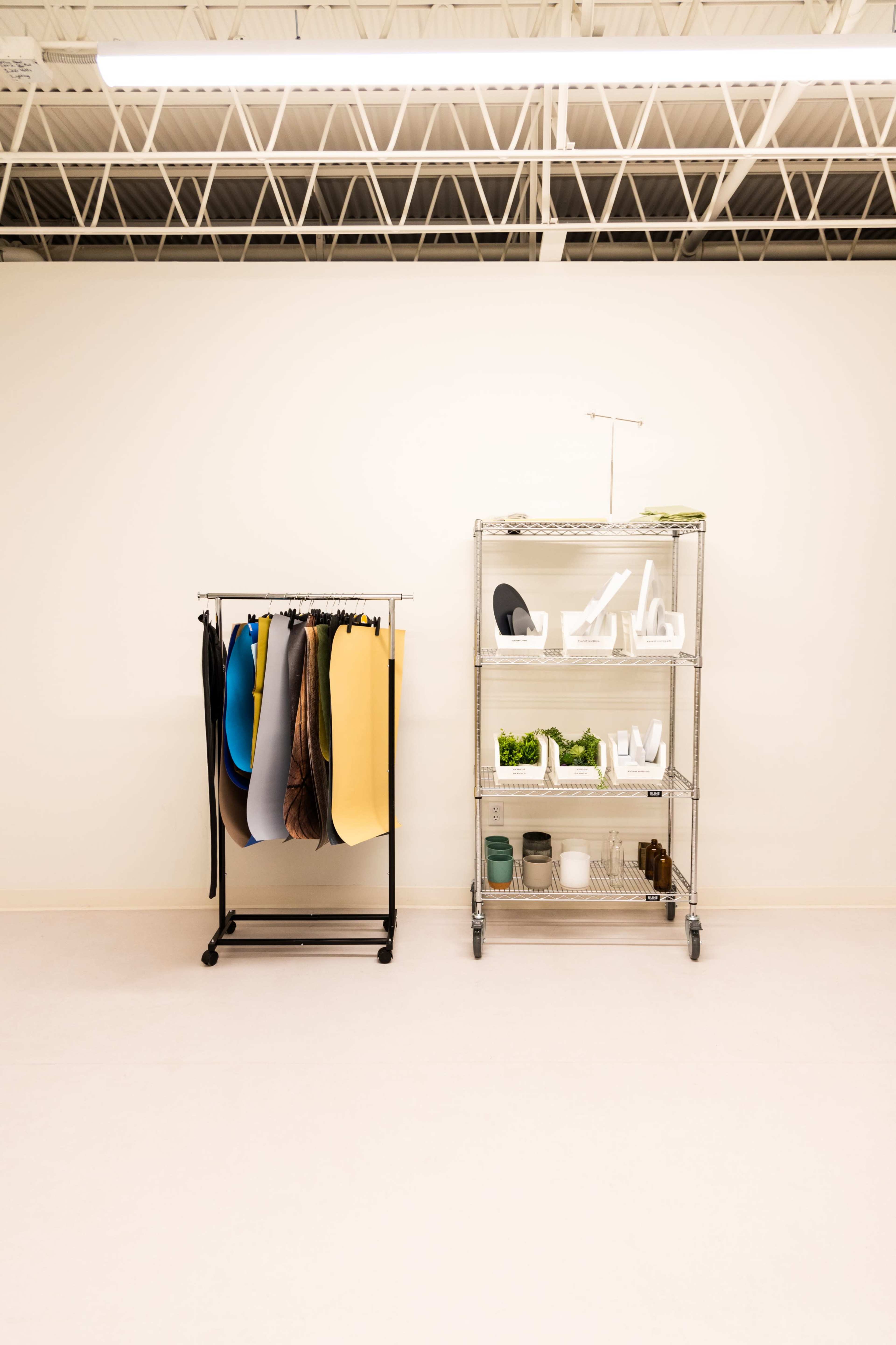A display area with two shelving units: one holds rolls of colorful materials, while the other contains various organizational items and plants.