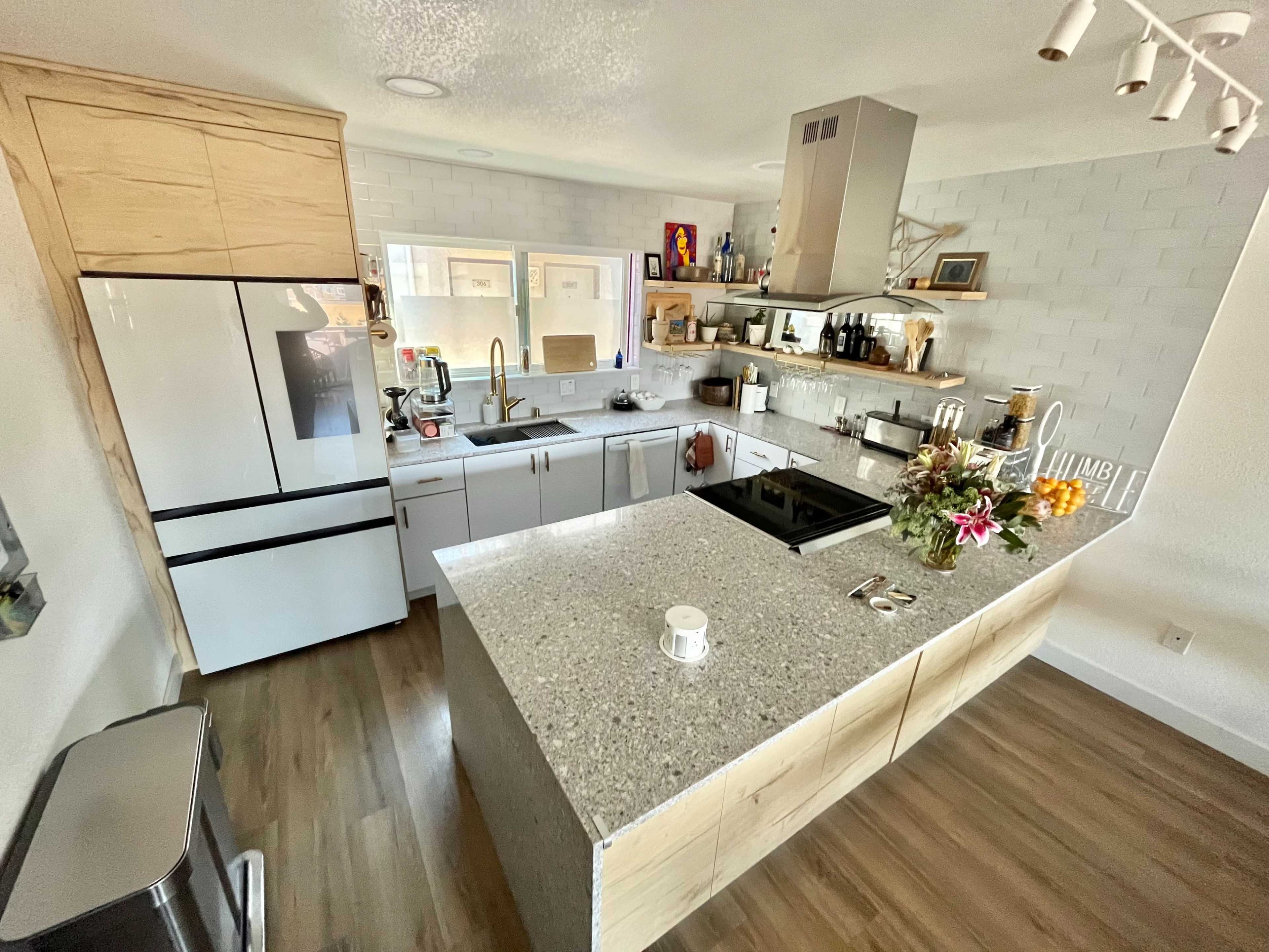 A modern kitchen features a large island with a sink, a cooktop, and wooden cabinetry, along with an organized arrangement of appliances and decorative items on the countertops.