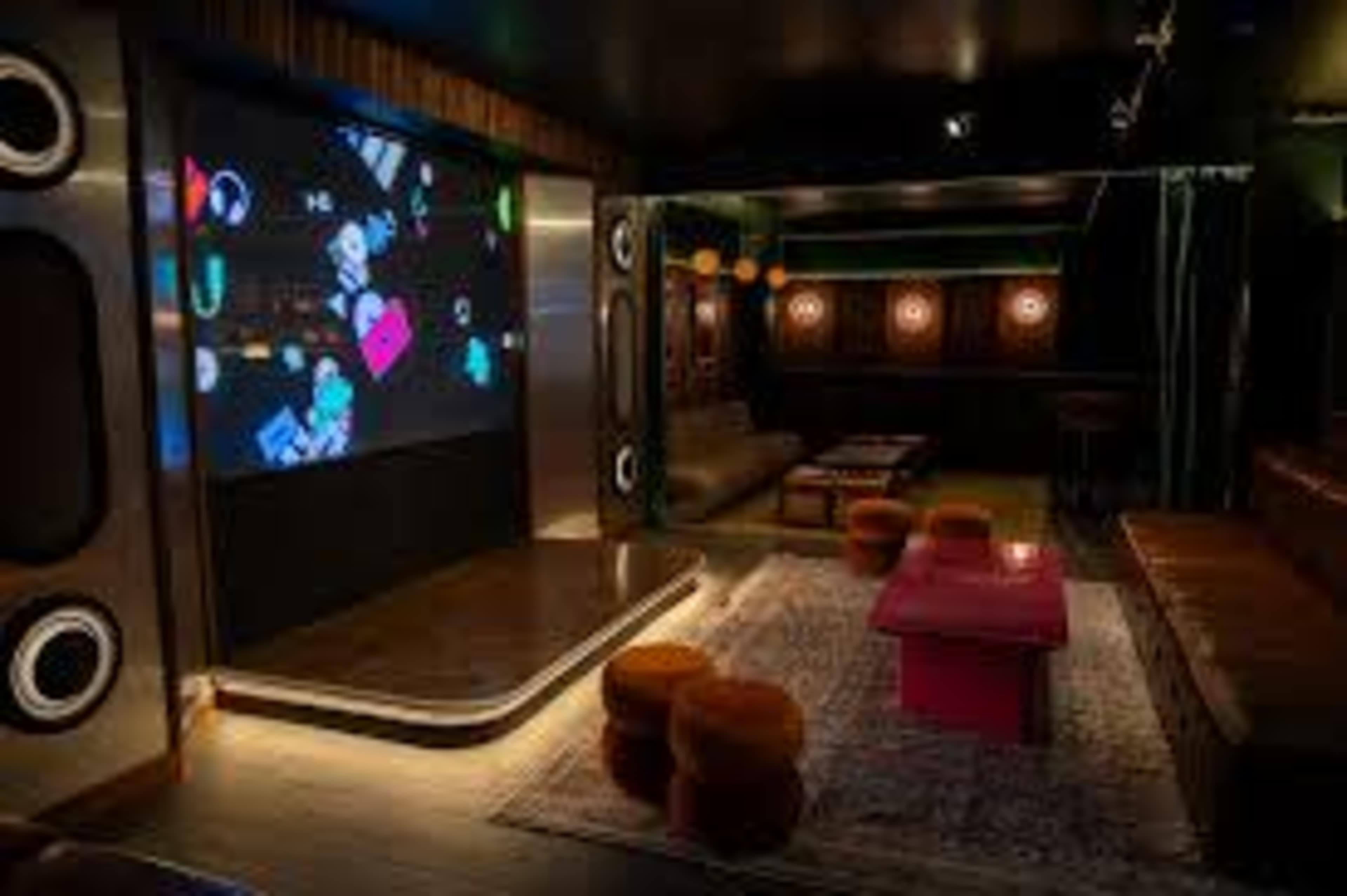The image shows a modern lounge area featuring a large projection screen, comfortable seating, and colorful accent furniture.