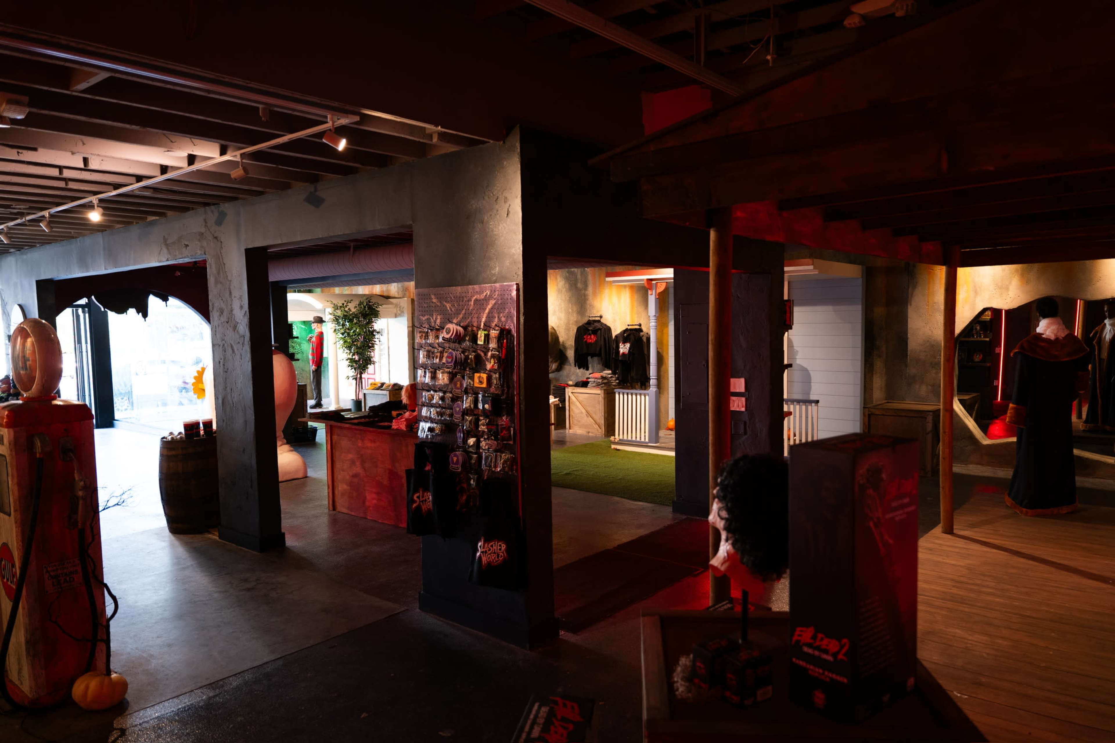 The image shows an indoor retail space with dark-themed decor, featuring merchandise displays, clothing racks, and various items related to a horror or Halloween theme.