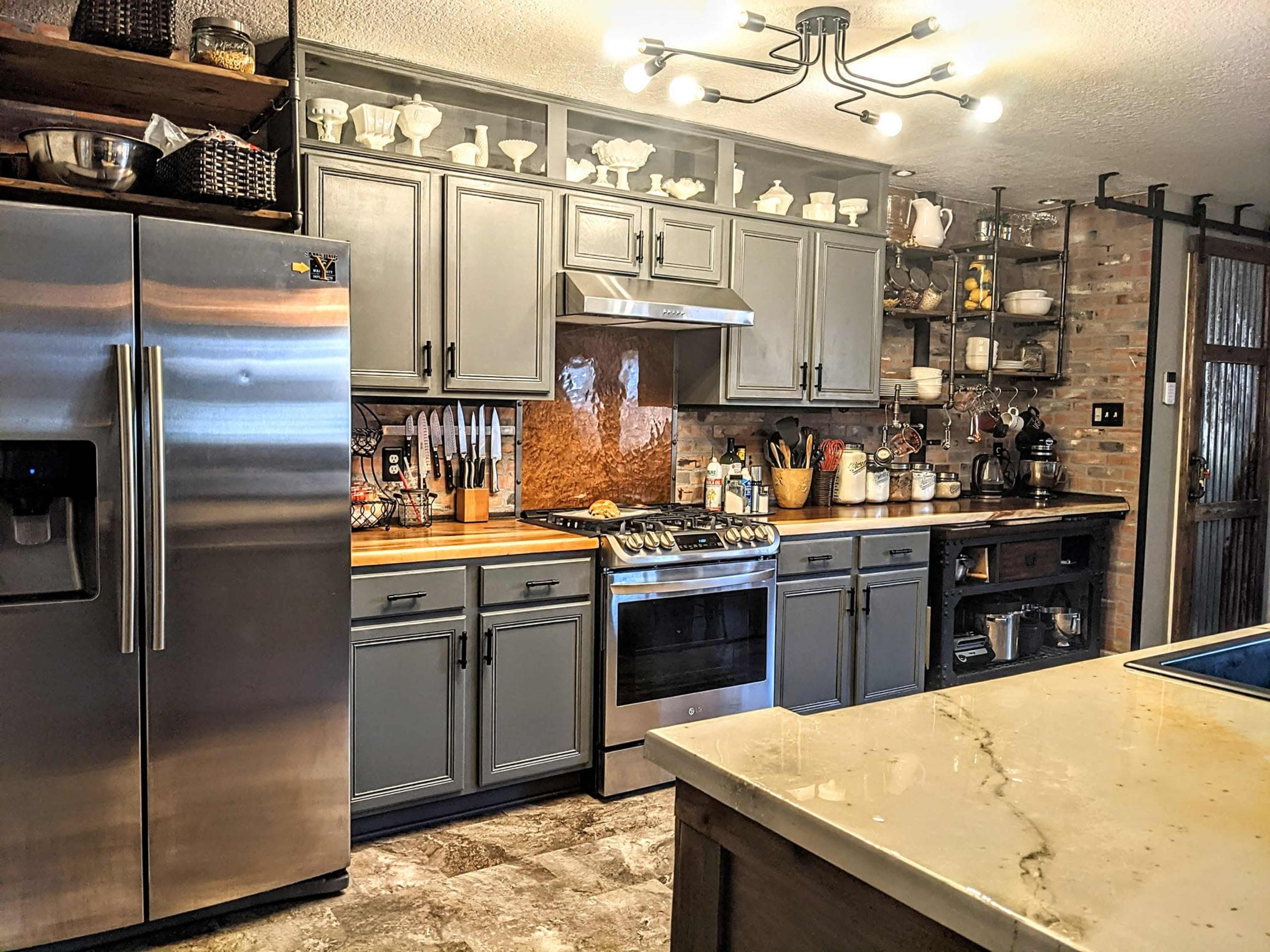 The image shows a modern kitchen featuring stainless steel appliances, gray cabinets, and a central island with a marble countertop.