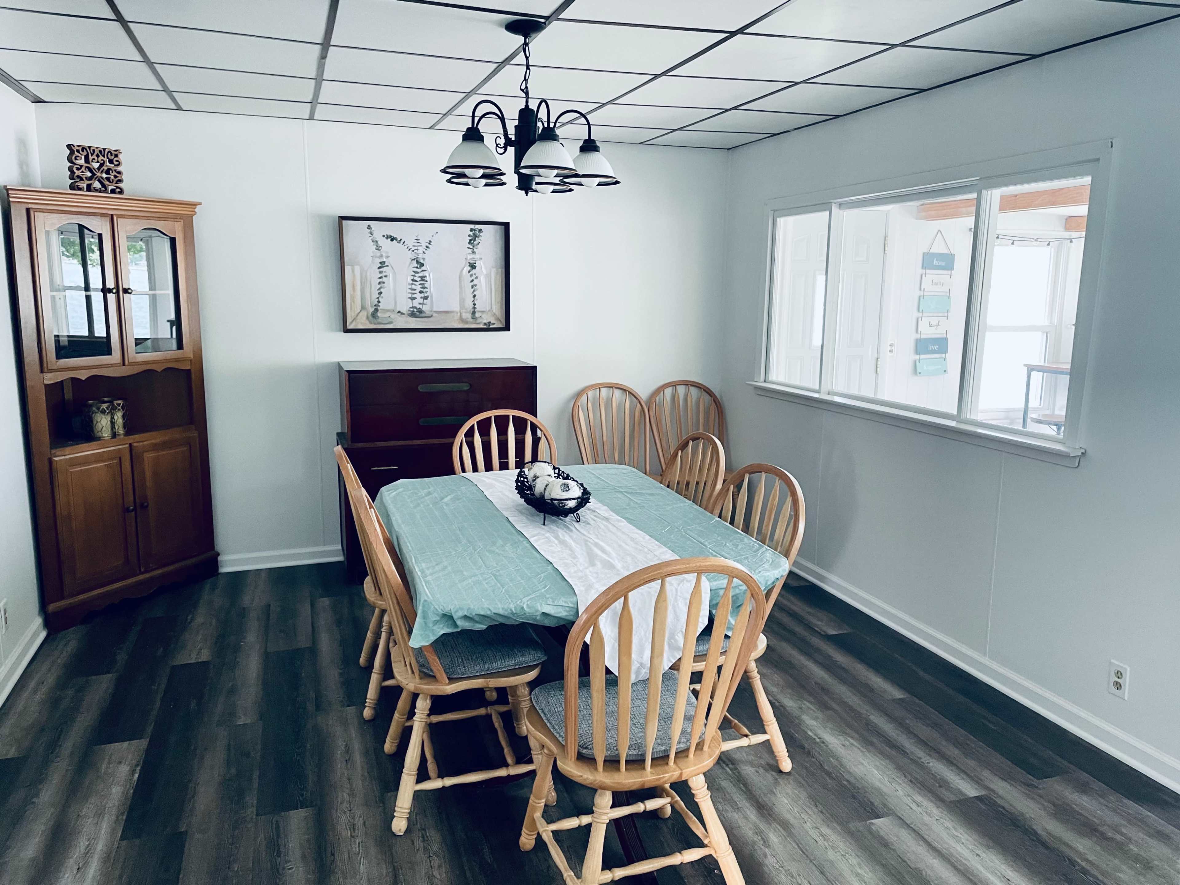 A dining area features a wooden table surrounded by six chairs, with a cabinet and a sideboard against the walls.