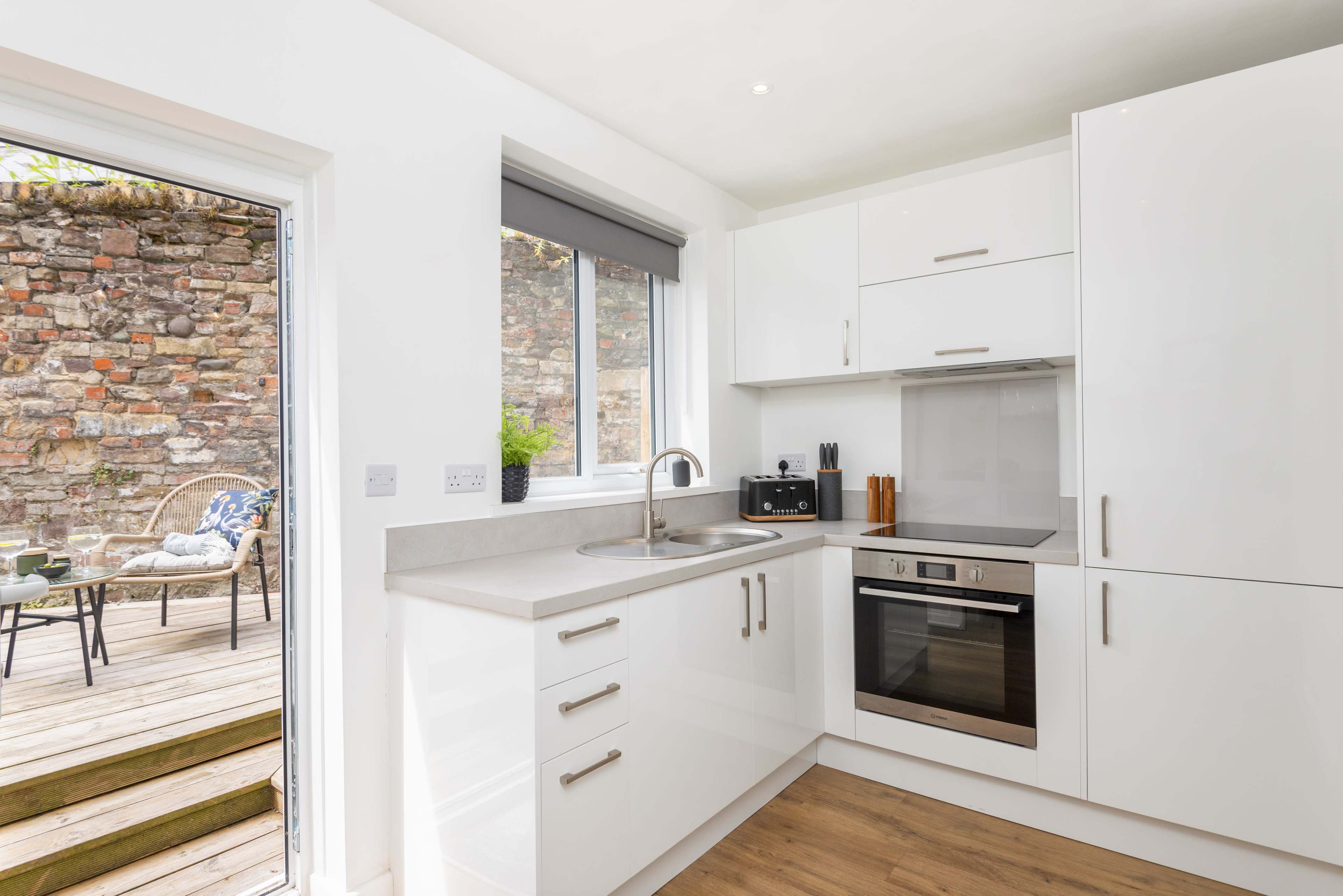 A modern kitchen features white cabinetry, a stainless steel oven, and a view of an outdoor deck area through a glass door.