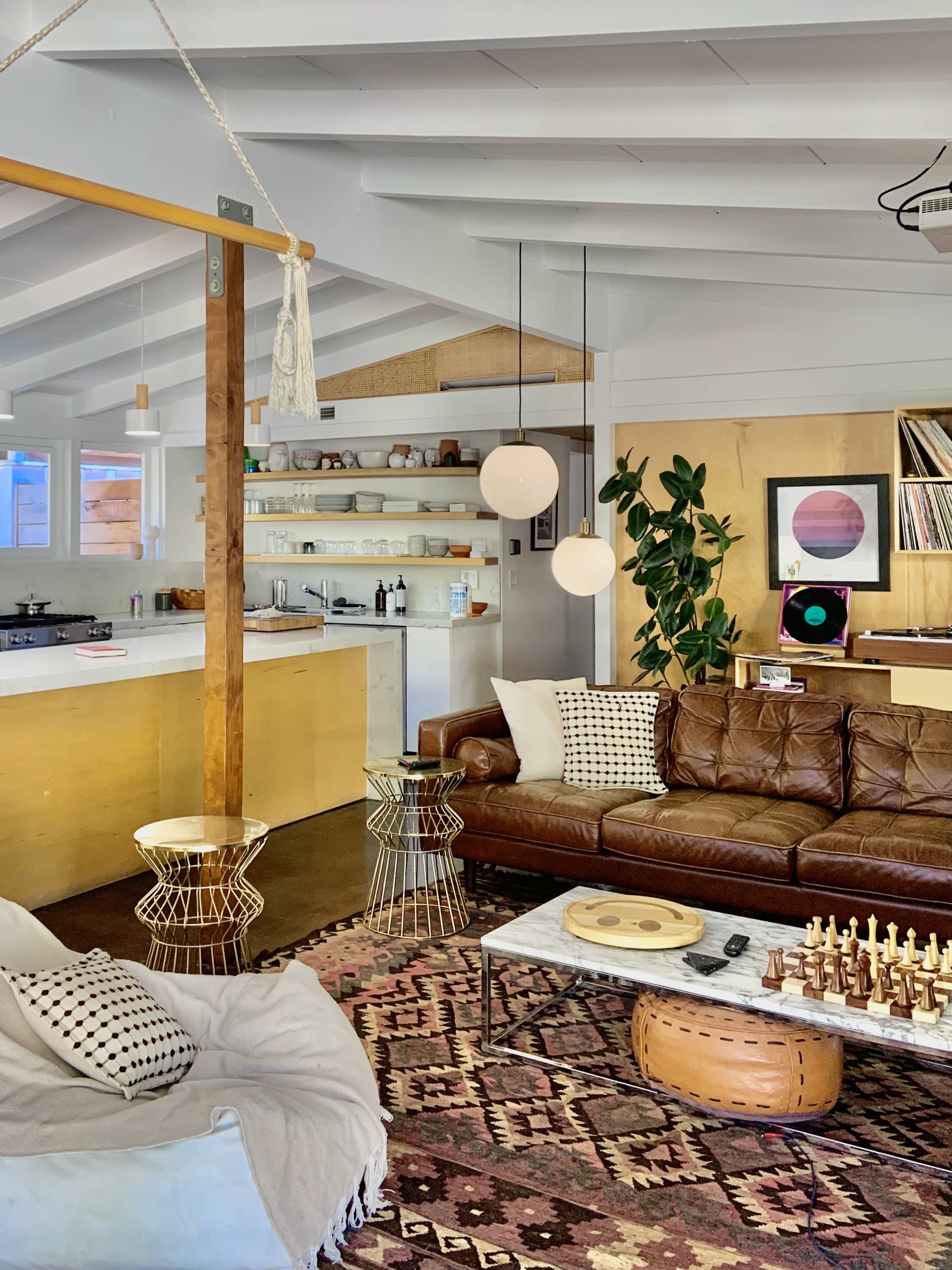 A cozy living area with a leather sofa, a marble coffee table, and a kitchen area in the background with shelves and a plant.