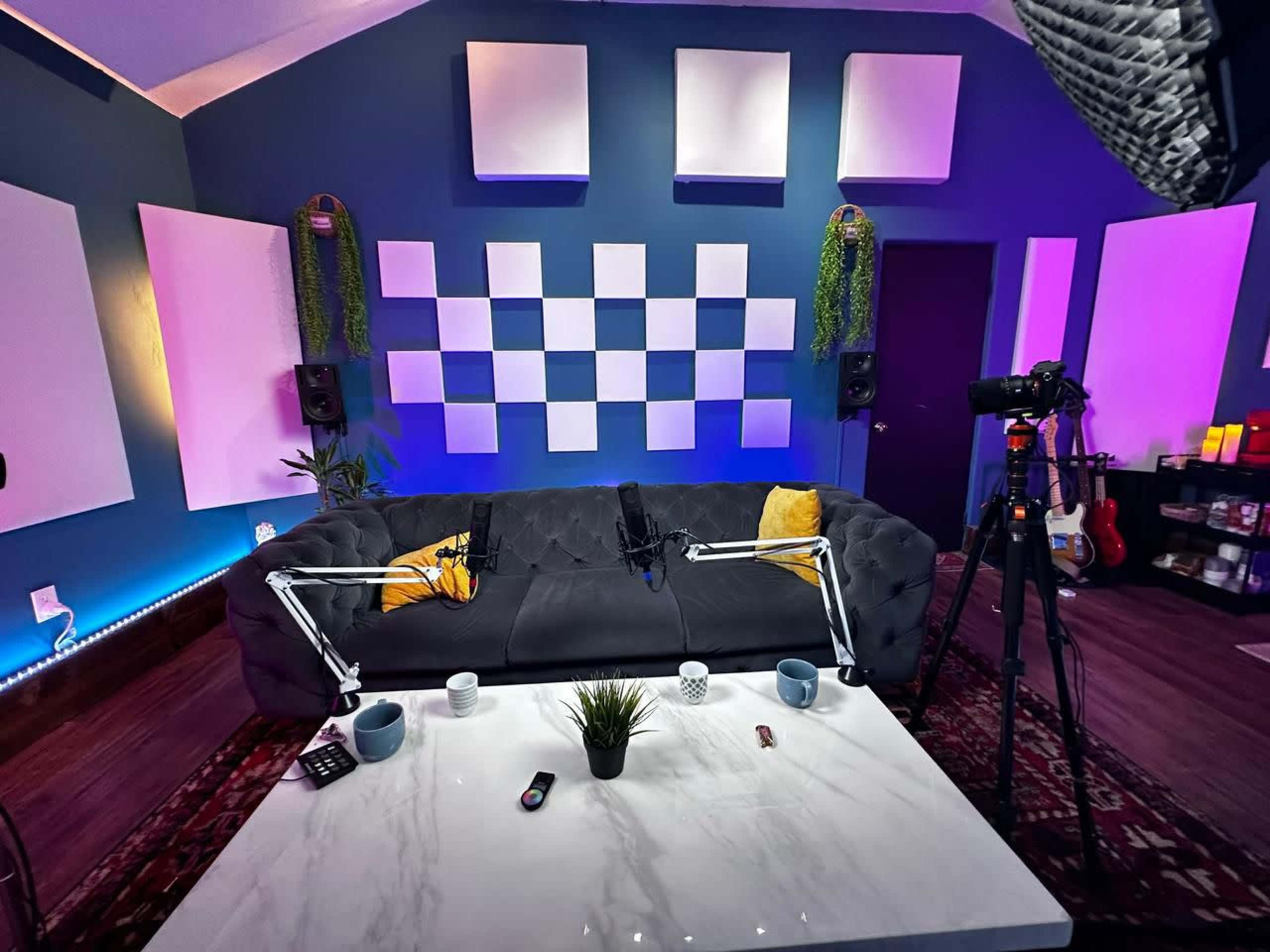 A modern living room setup featuring a dark couch, a marble table, and ambient lighting on the walls, with audio equipment set up for recording.