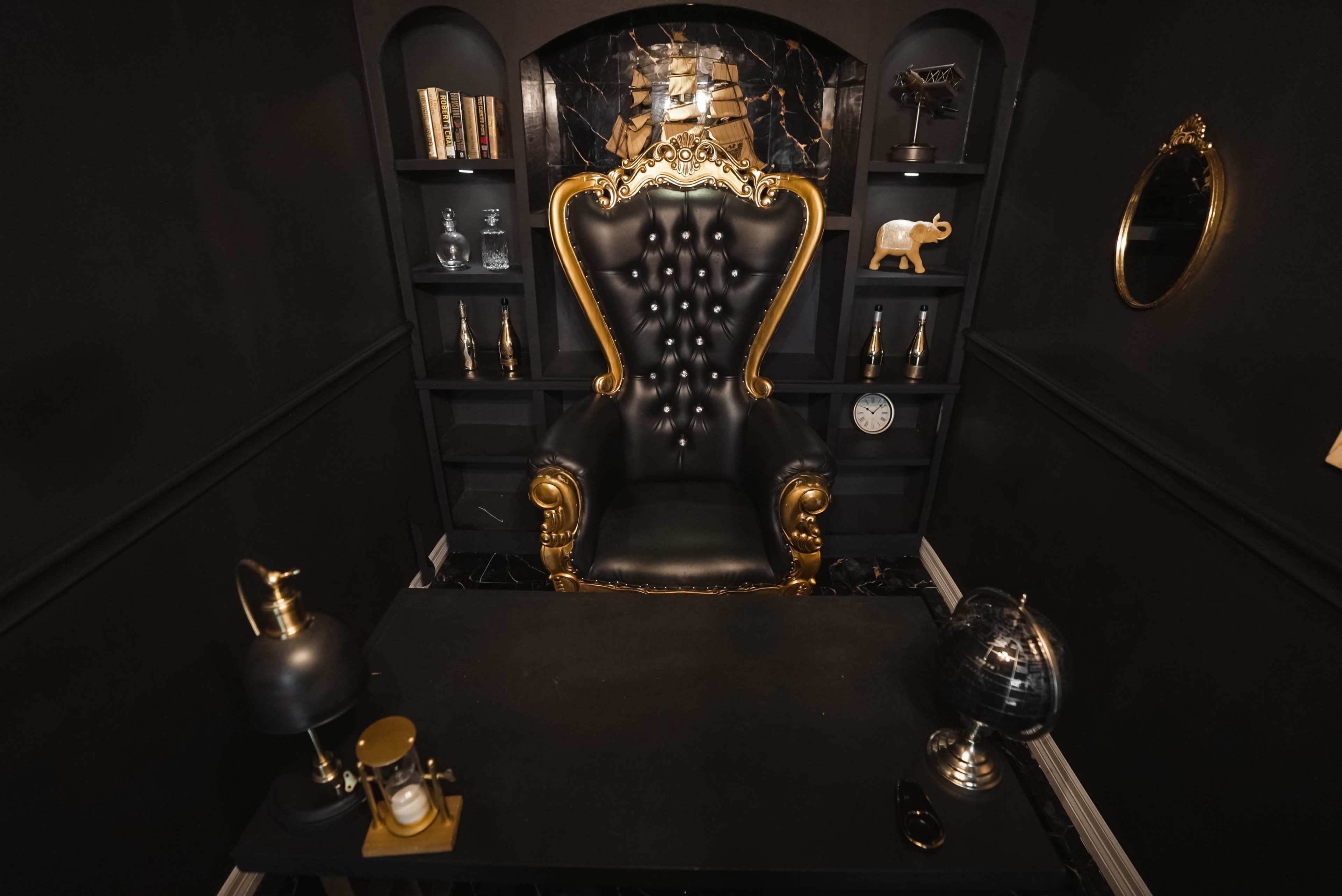 The image shows a dark, elegant office space featuring a large black and gold throne-like chair, a black table, and various decorative items on built-in shelves.