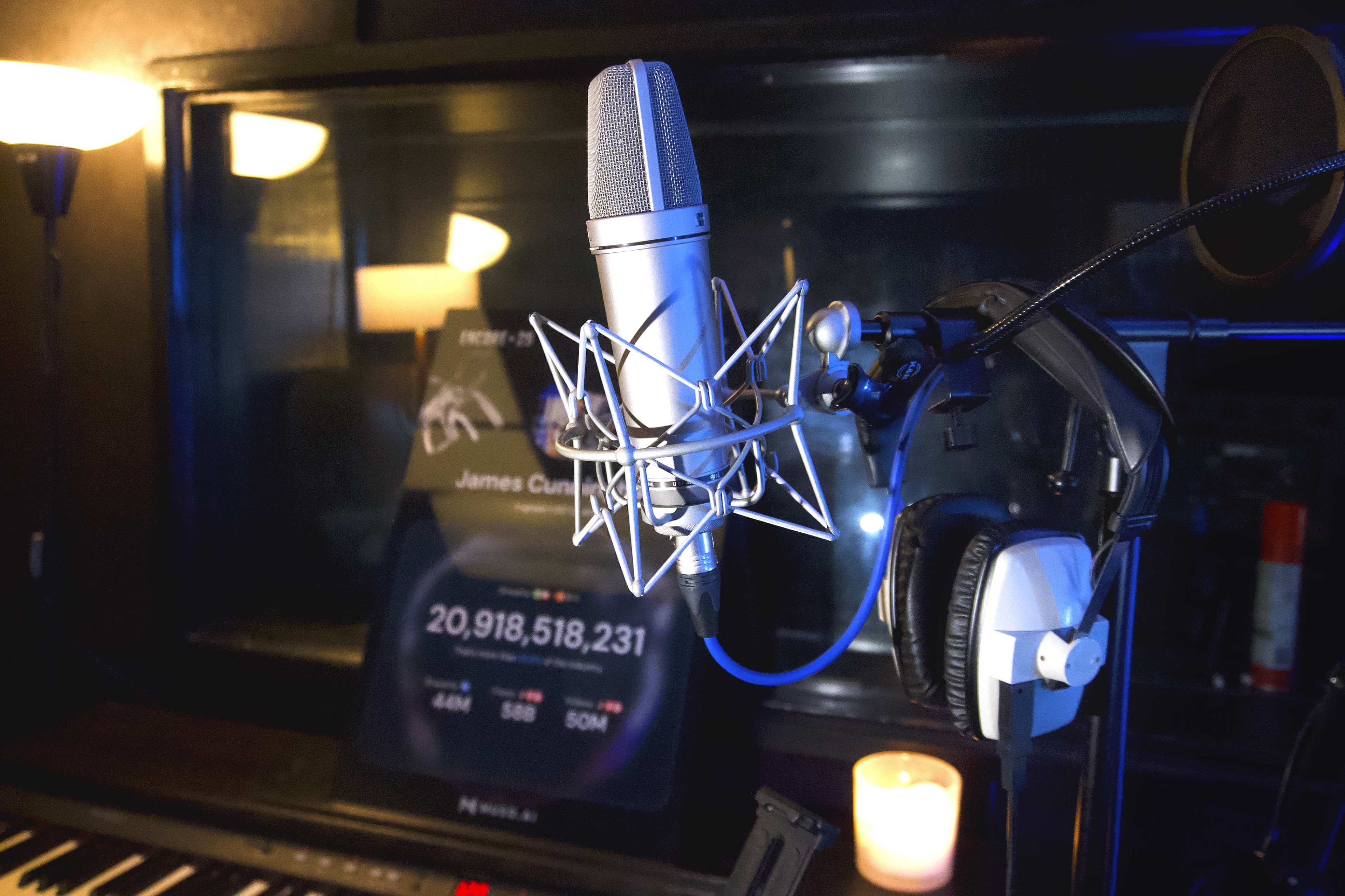 A microphone is positioned in a recording studio with a digital display in the background showing statistics related to an artist.