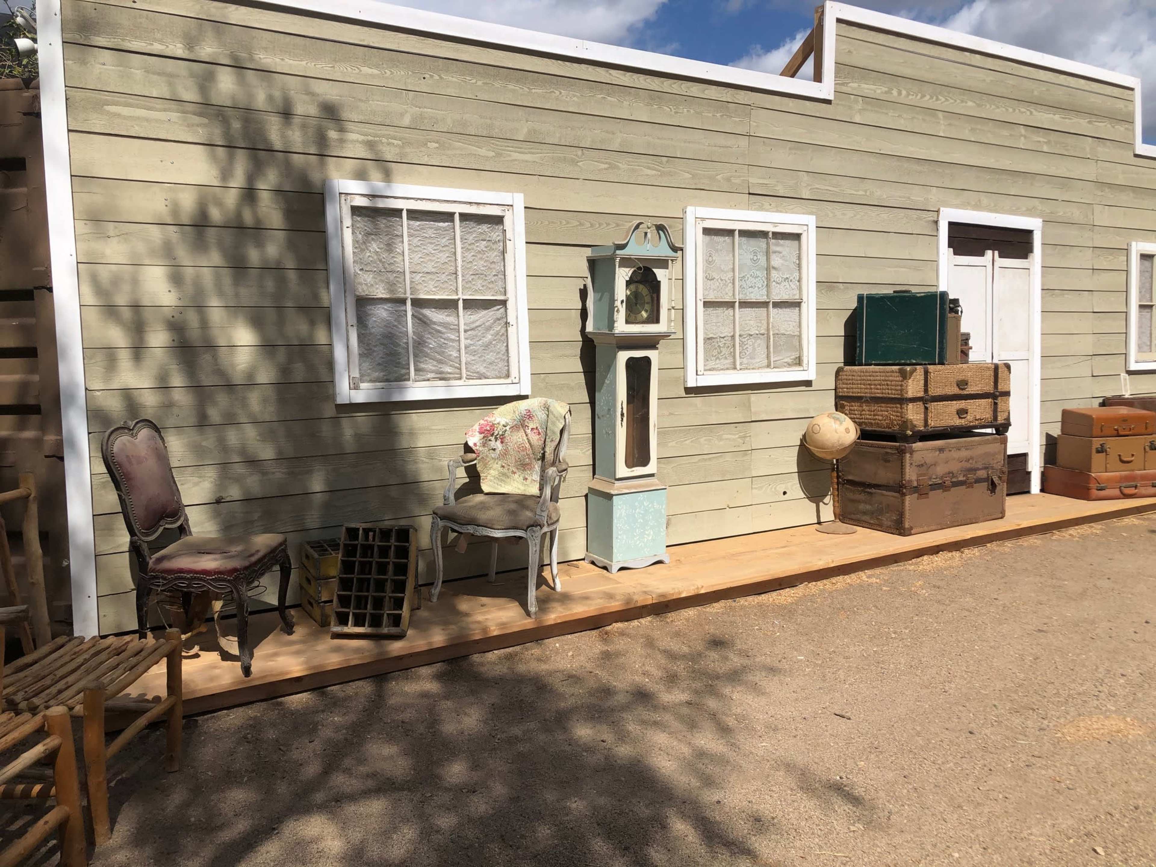 A wooden building facade with various pieces of antique furniture, including chairs and boxes, arranged on a wooden platform in front.