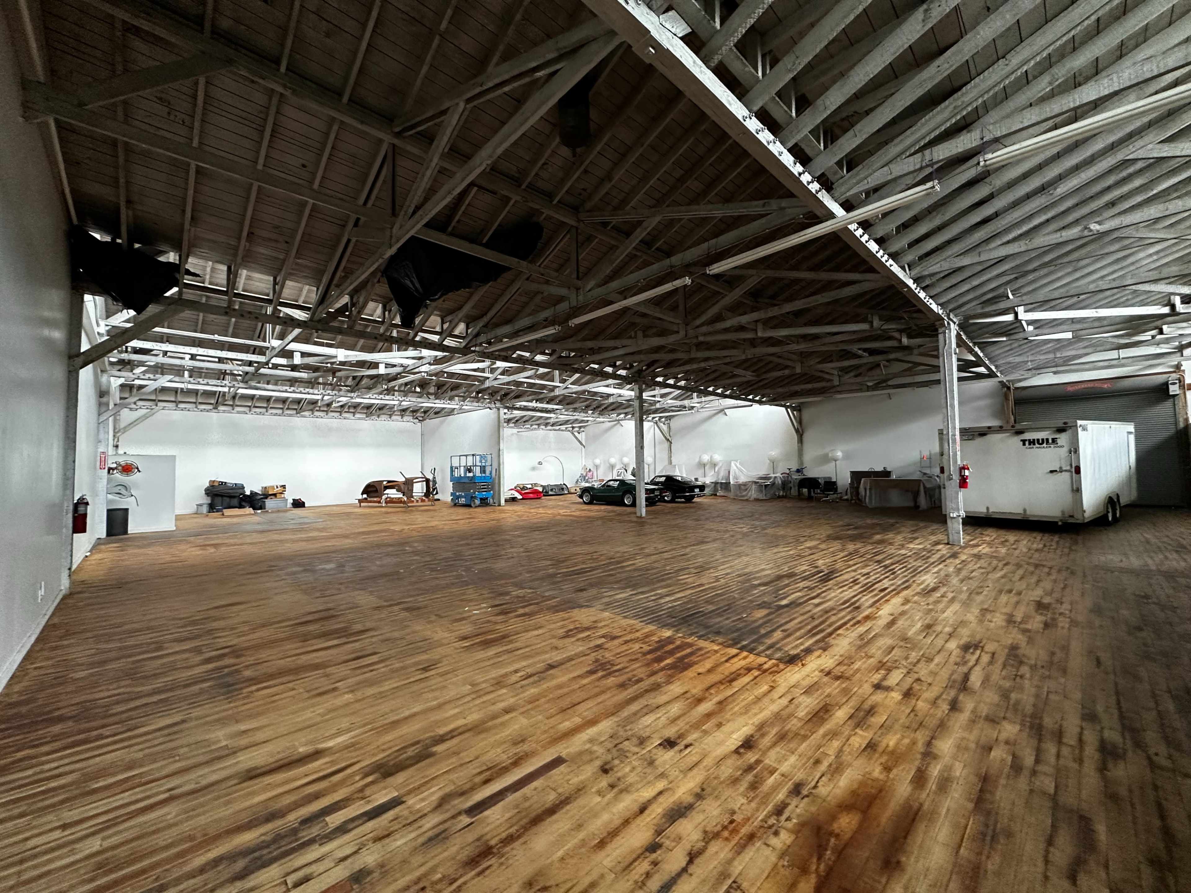 An empty industrial space with wooden floors, high ceilings, and various equipment along the walls.