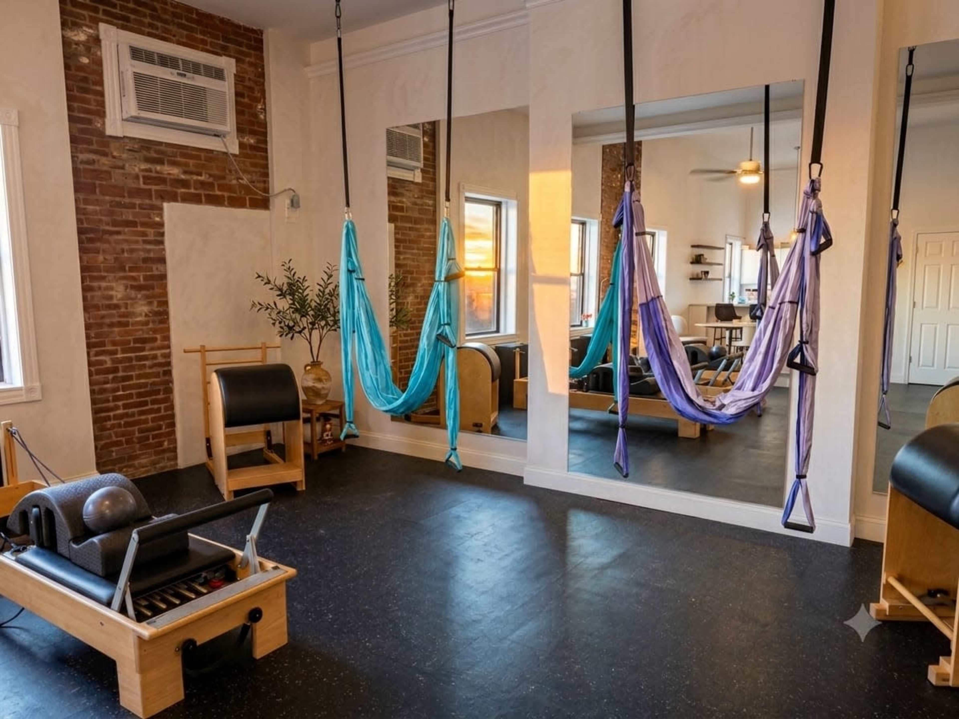 The image shows a fitness studio with hanging aerial silk hammocks, a Pilates reformer, and mirrors reflecting a well-lit interior.