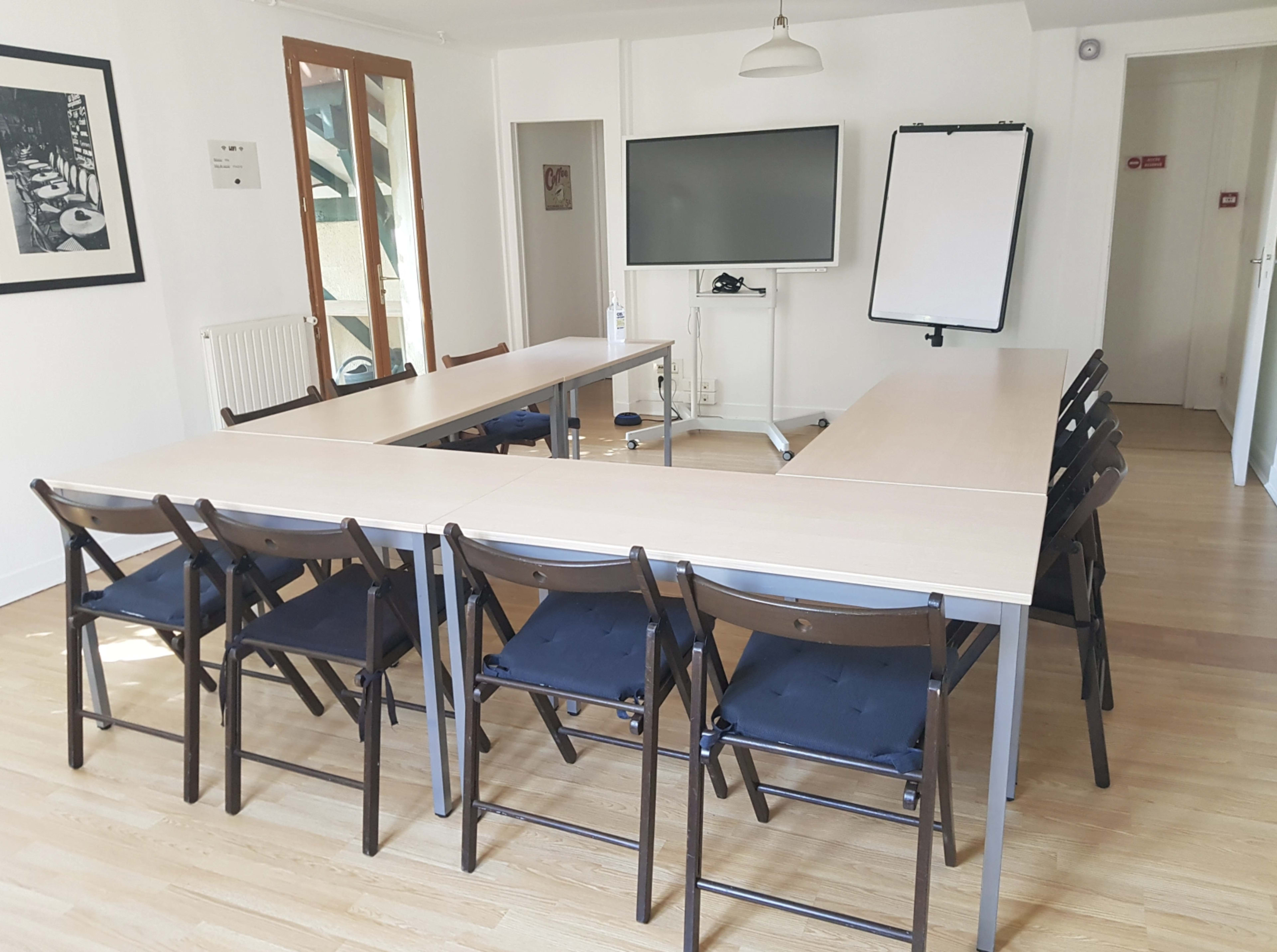 A conference room features a large rectangular table with several chairs arranged around it, a large screen at one end, and a whiteboard nearby.