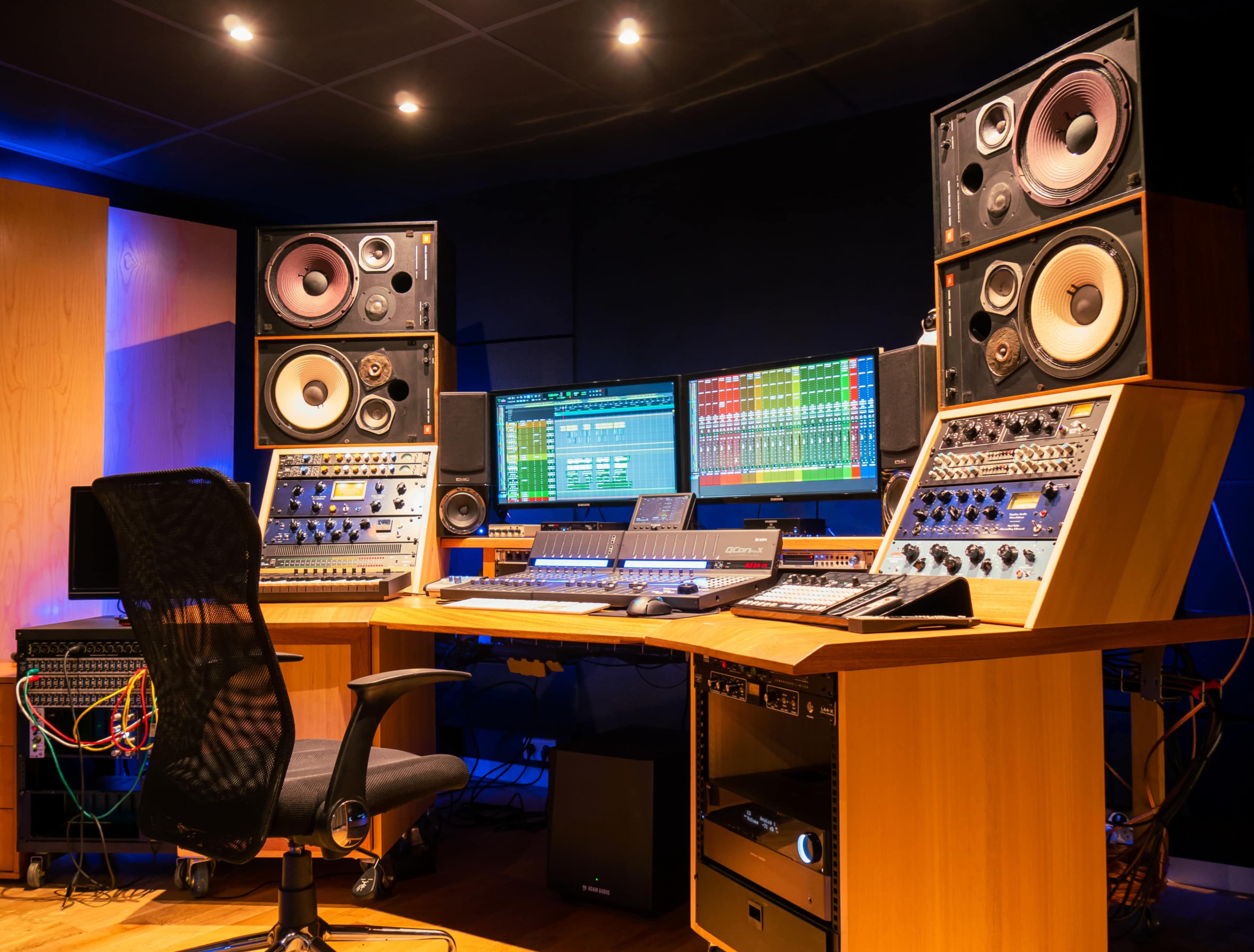 A modern recording studio with a mixing console, monitors, and audio equipment arranged around a central workstation.