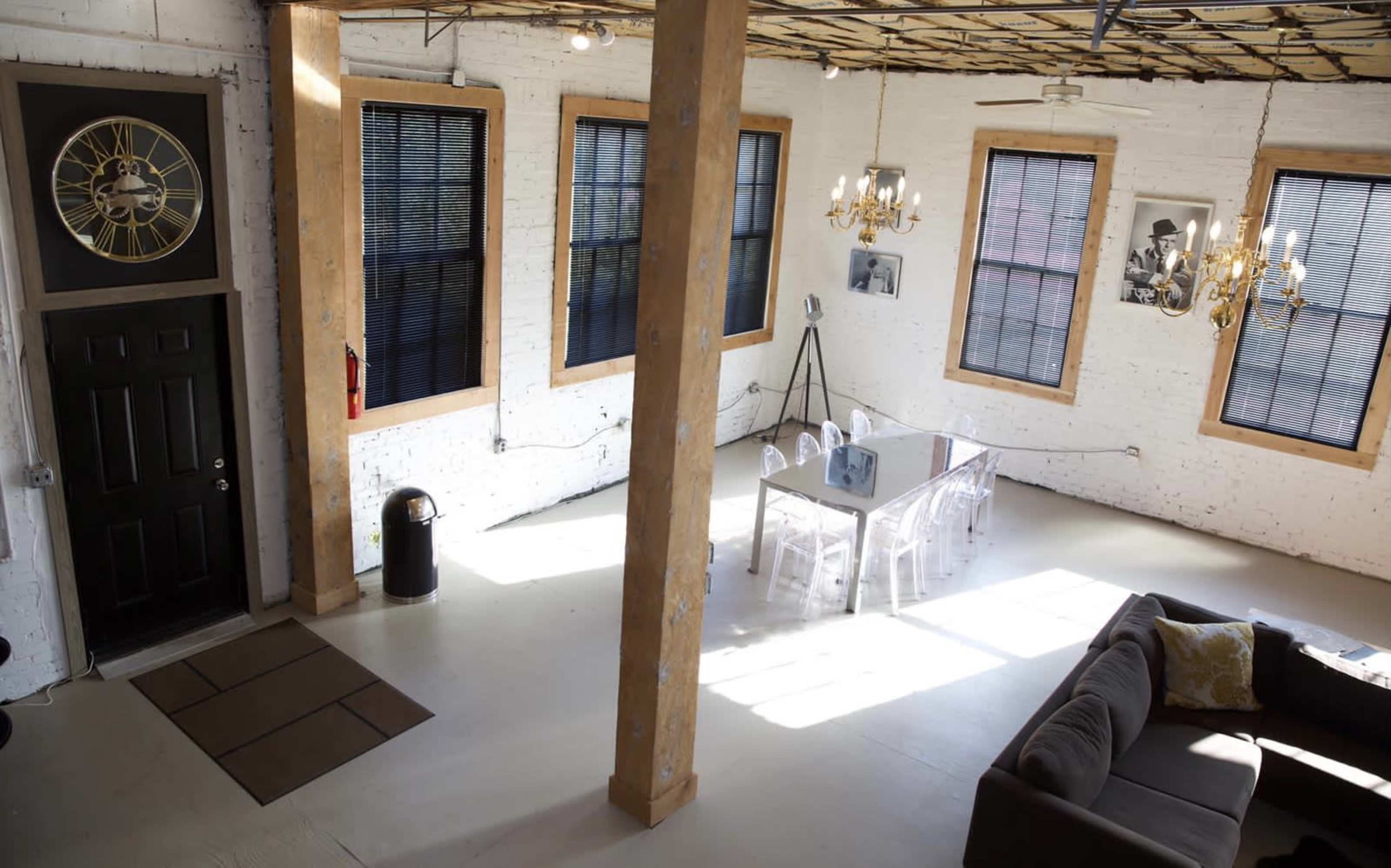 A spacious, modern interior with exposed brick walls, a dining table in the center, and large windows allowing natural light to enter.