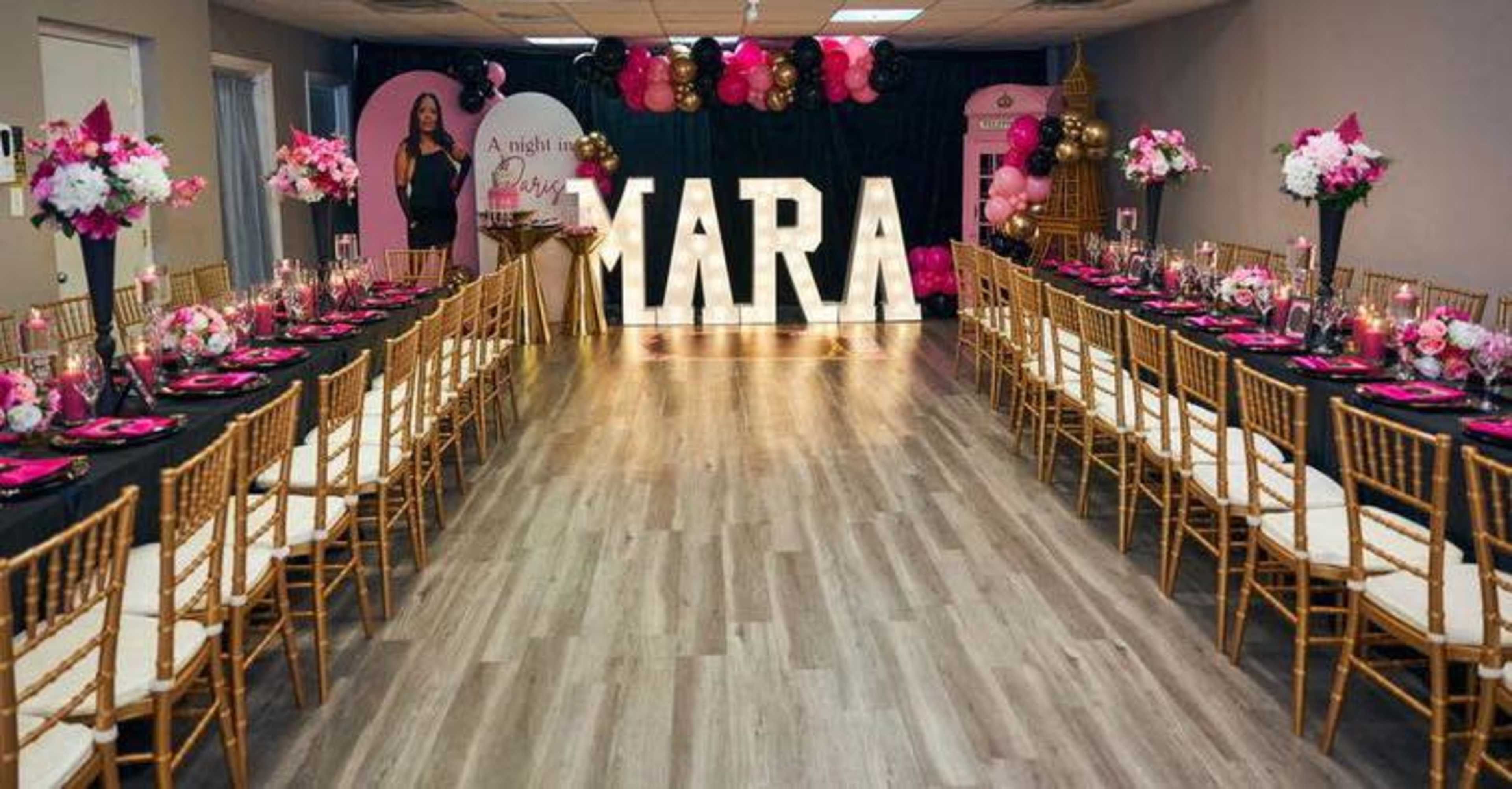 A decorated event space with a long dining setup featuring floral centerpieces and large illuminated letters spelling "MARA."