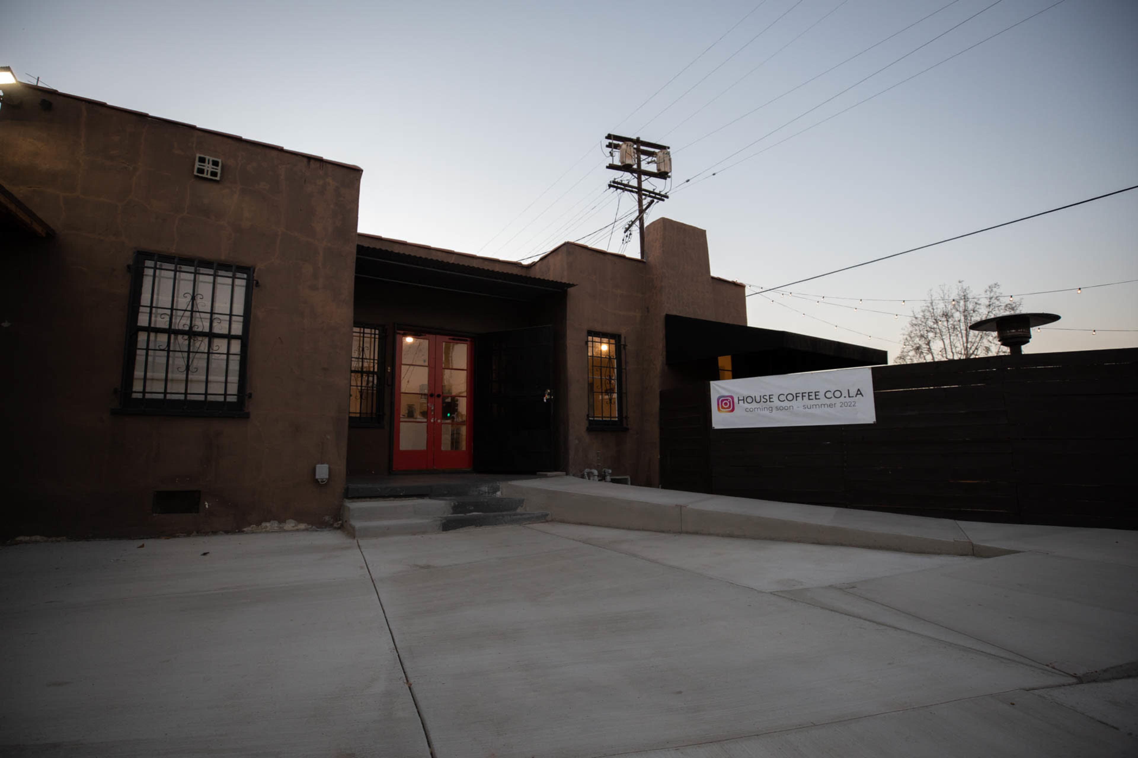 A coffee shop with a red door and a sign reading "House Coffee Co LA," surrounded by a concrete walkway and power lines in the background.