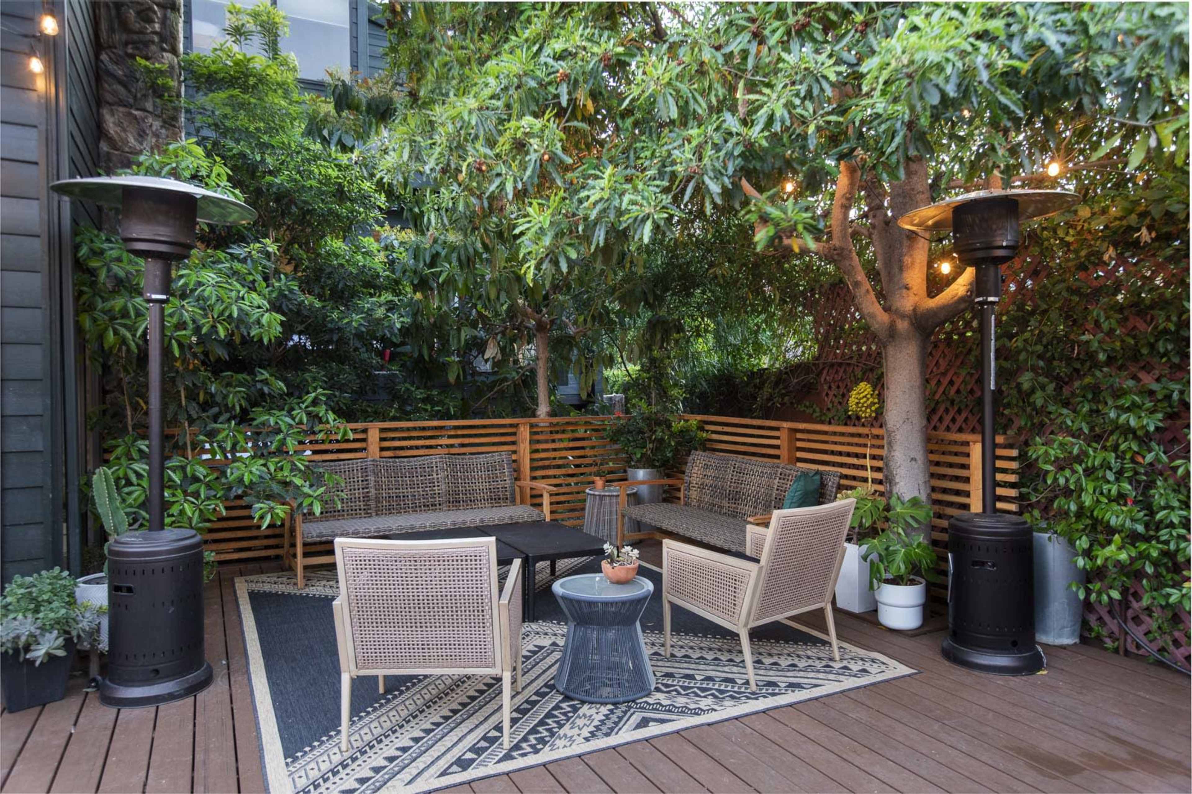 A well-furnished outdoor seating area is surrounded by lush greenery and features two patio heaters on a wooden deck.