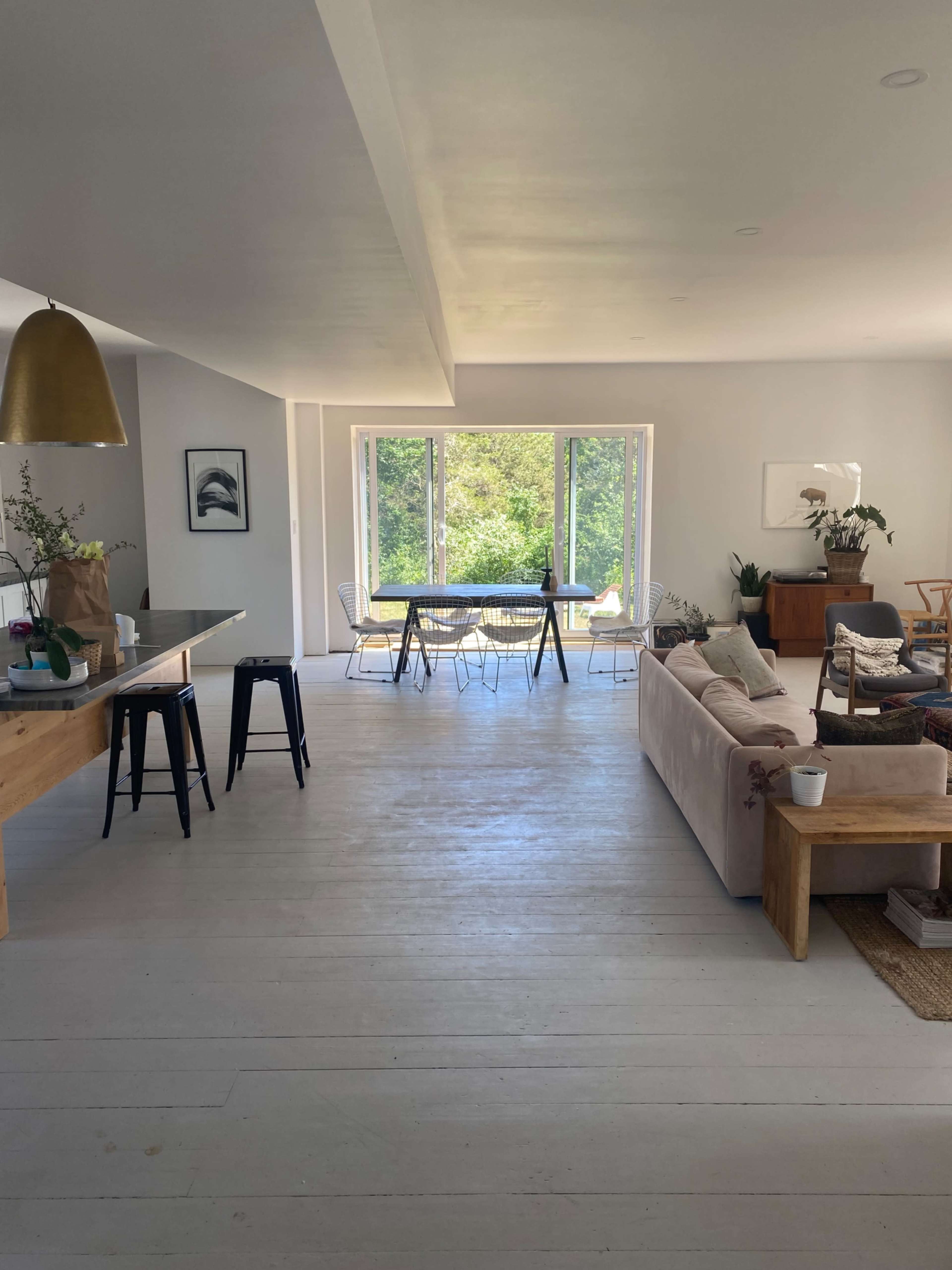 A modern living space featuring an open layout with a dining area and large windows overlooking greenery.