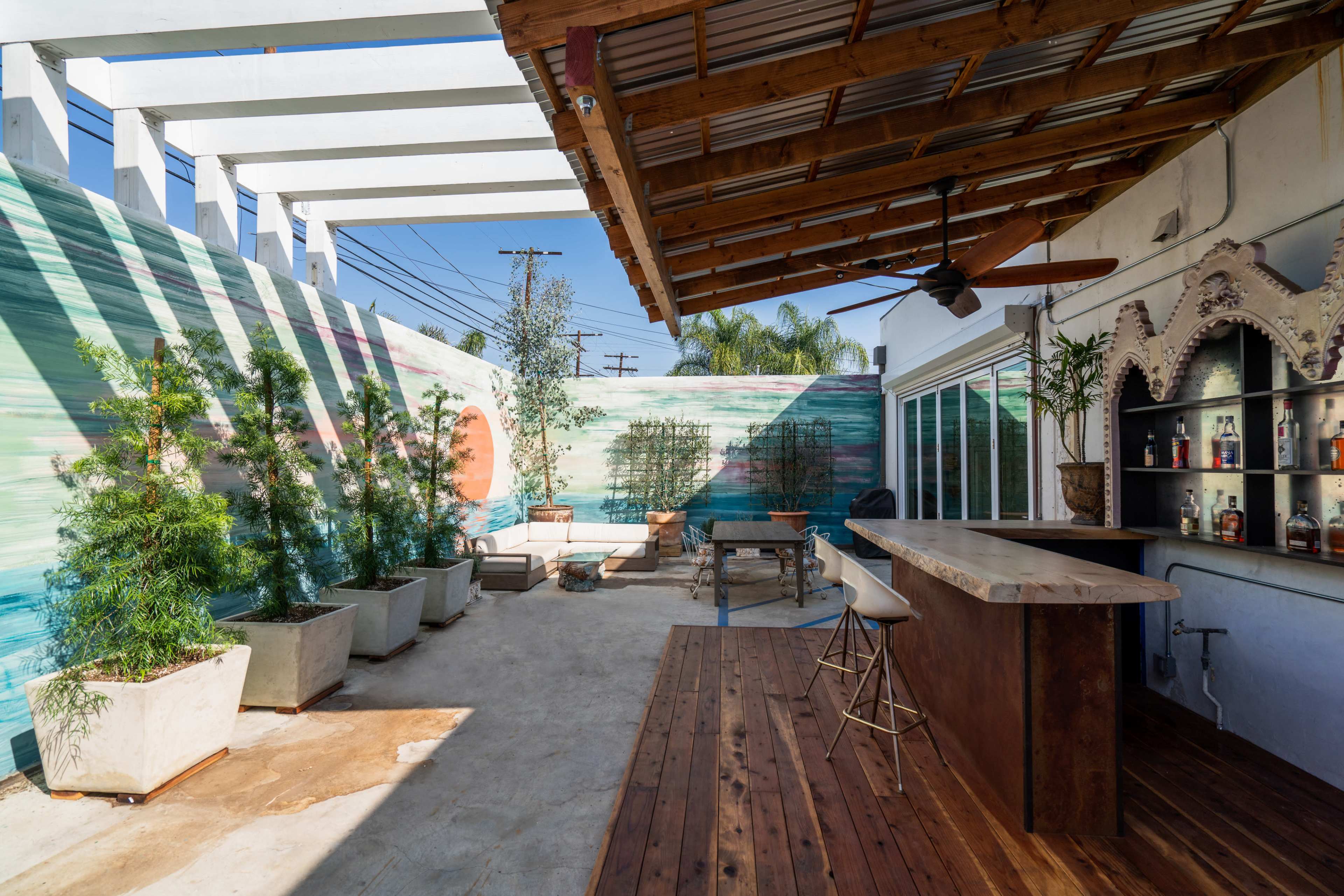 An outdoor patio area with a wooden bar, planters, and a colorful mural on the wall.