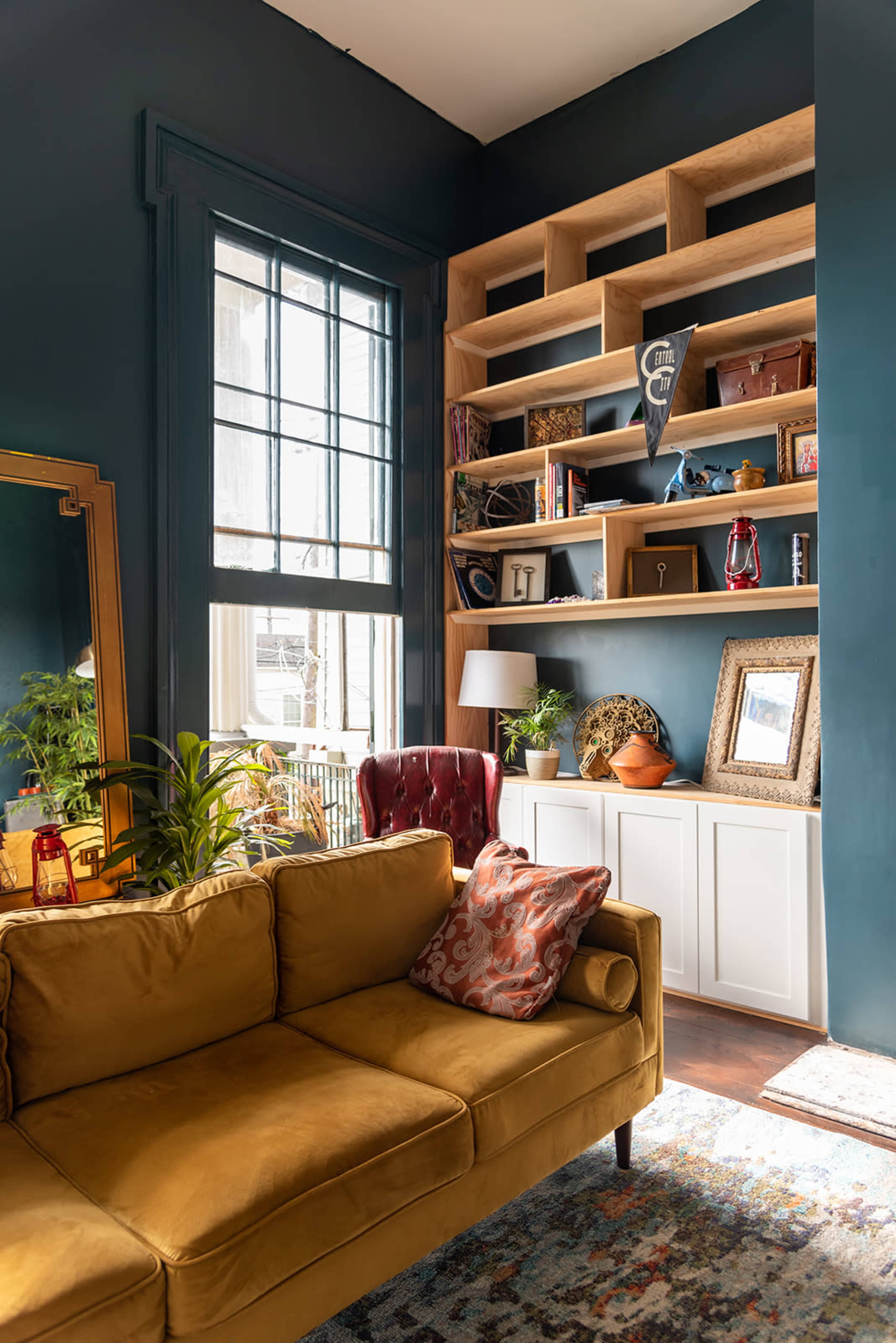 A yellow couch is positioned in a living room featuring teal walls and a built-in shelf displaying decor items.